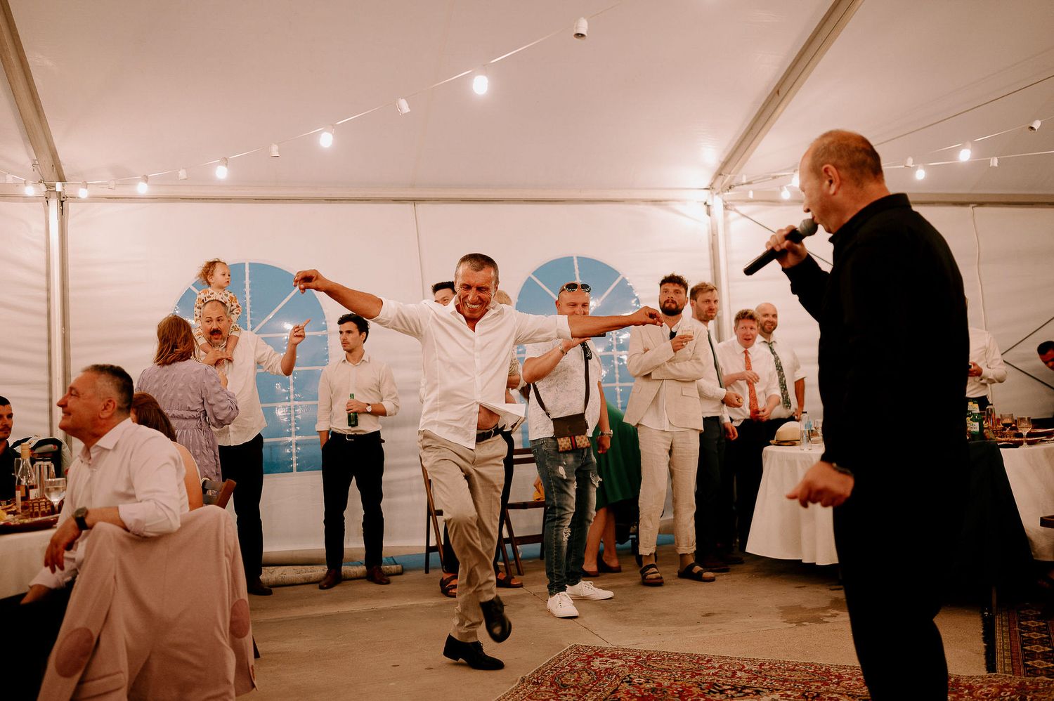 Wedding reception under a white tent with string lights and dancing guests.