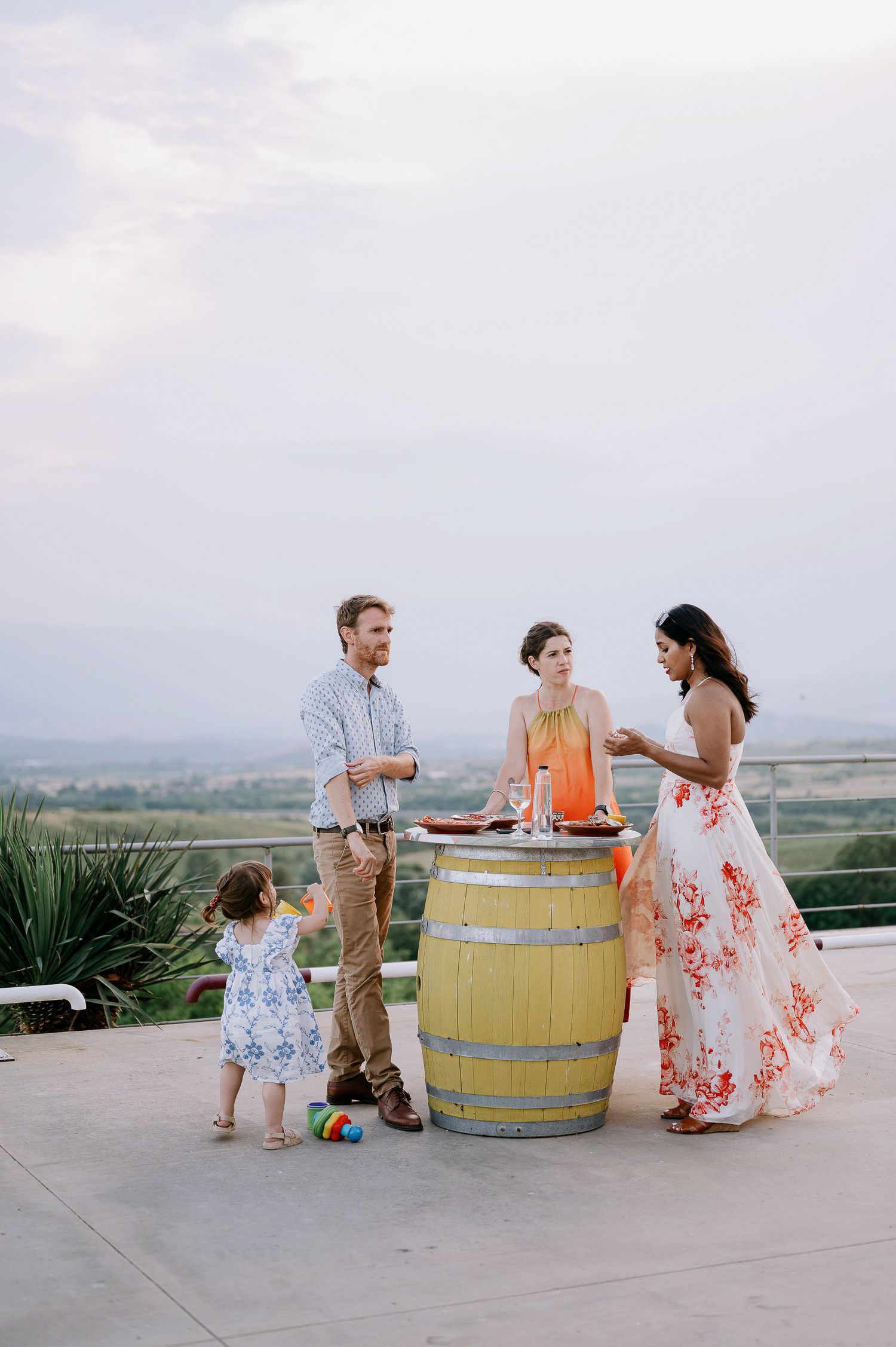 Outdoor celebration with guests mingling around wooden barrels on a scenic terrace.