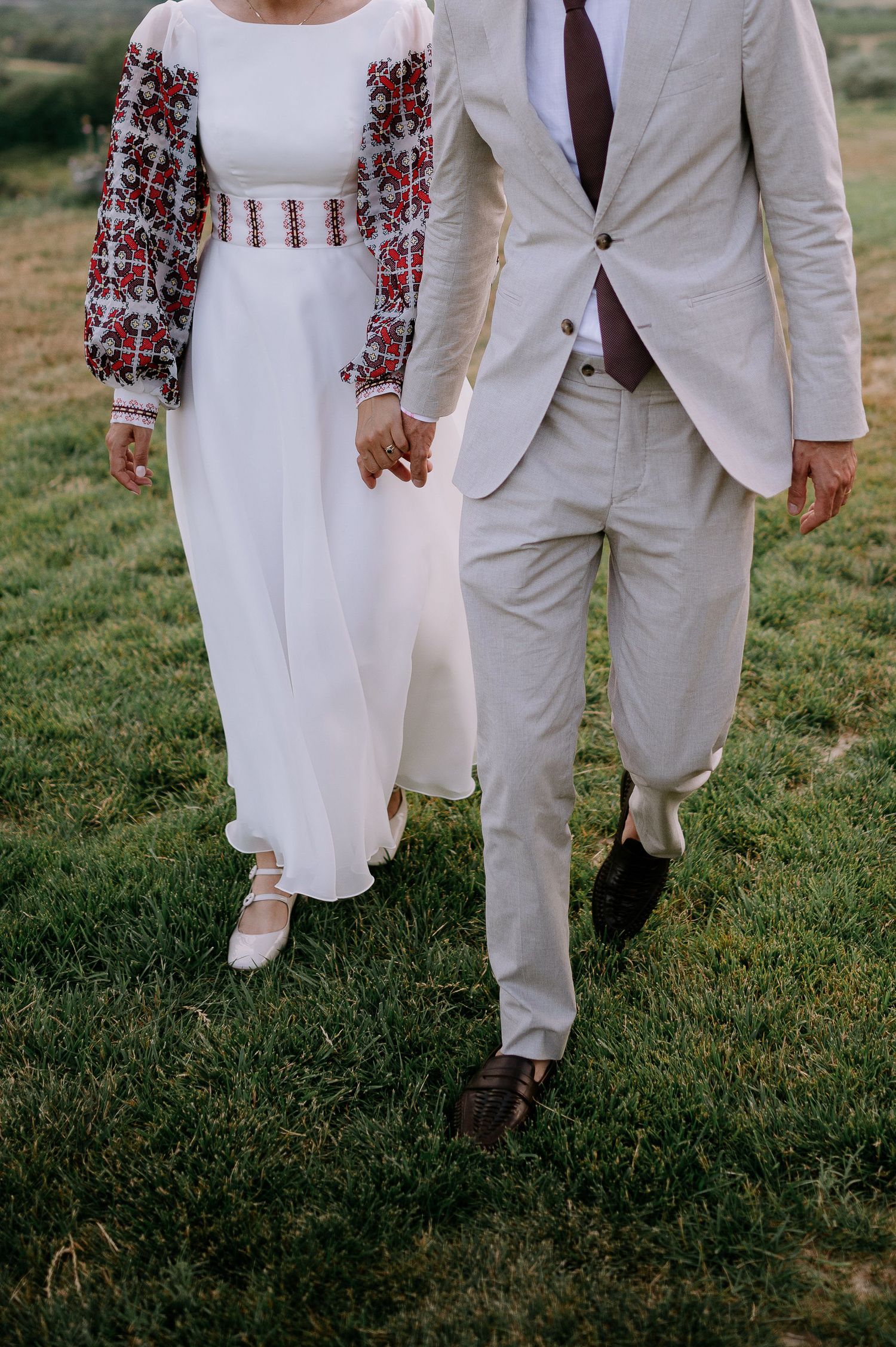 Close-up of couple walking together showing traditional embroidered dress and light suit details.