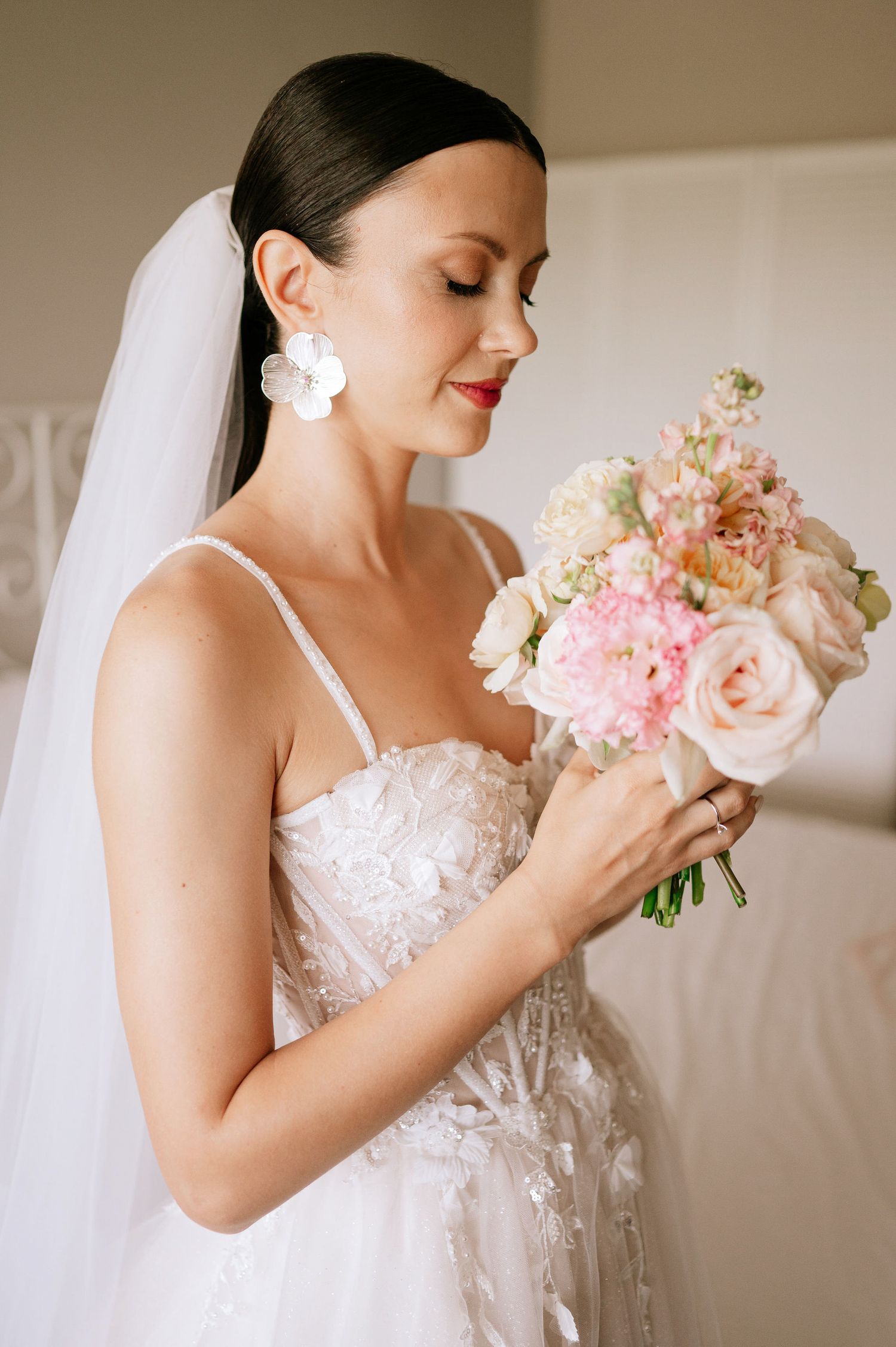 Bride holding a soft pink and peach bouquet while wearing a delicate lace wedding gown.