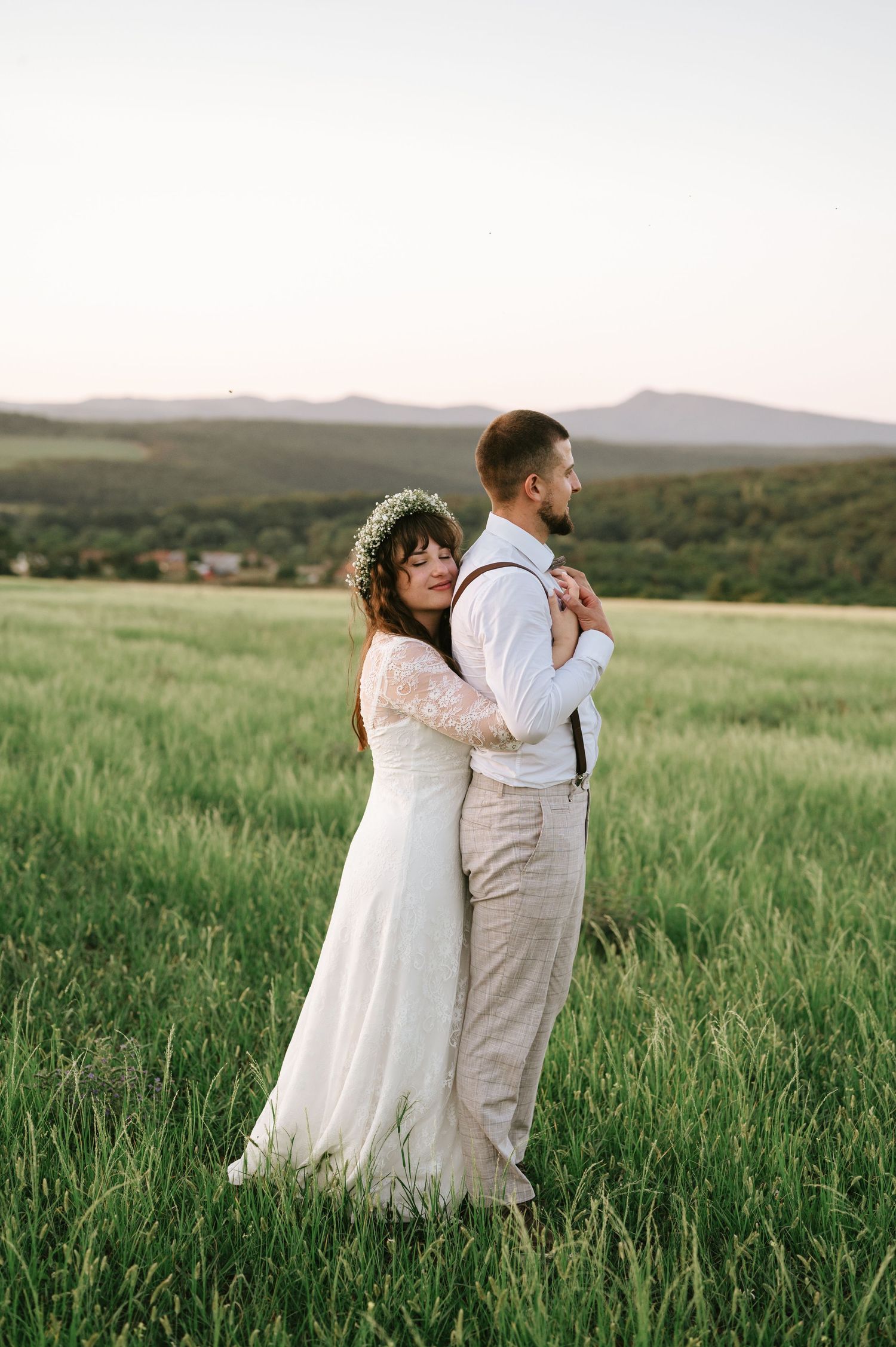 A tender moment between newlyweds in a scenic mountain field at sunset.