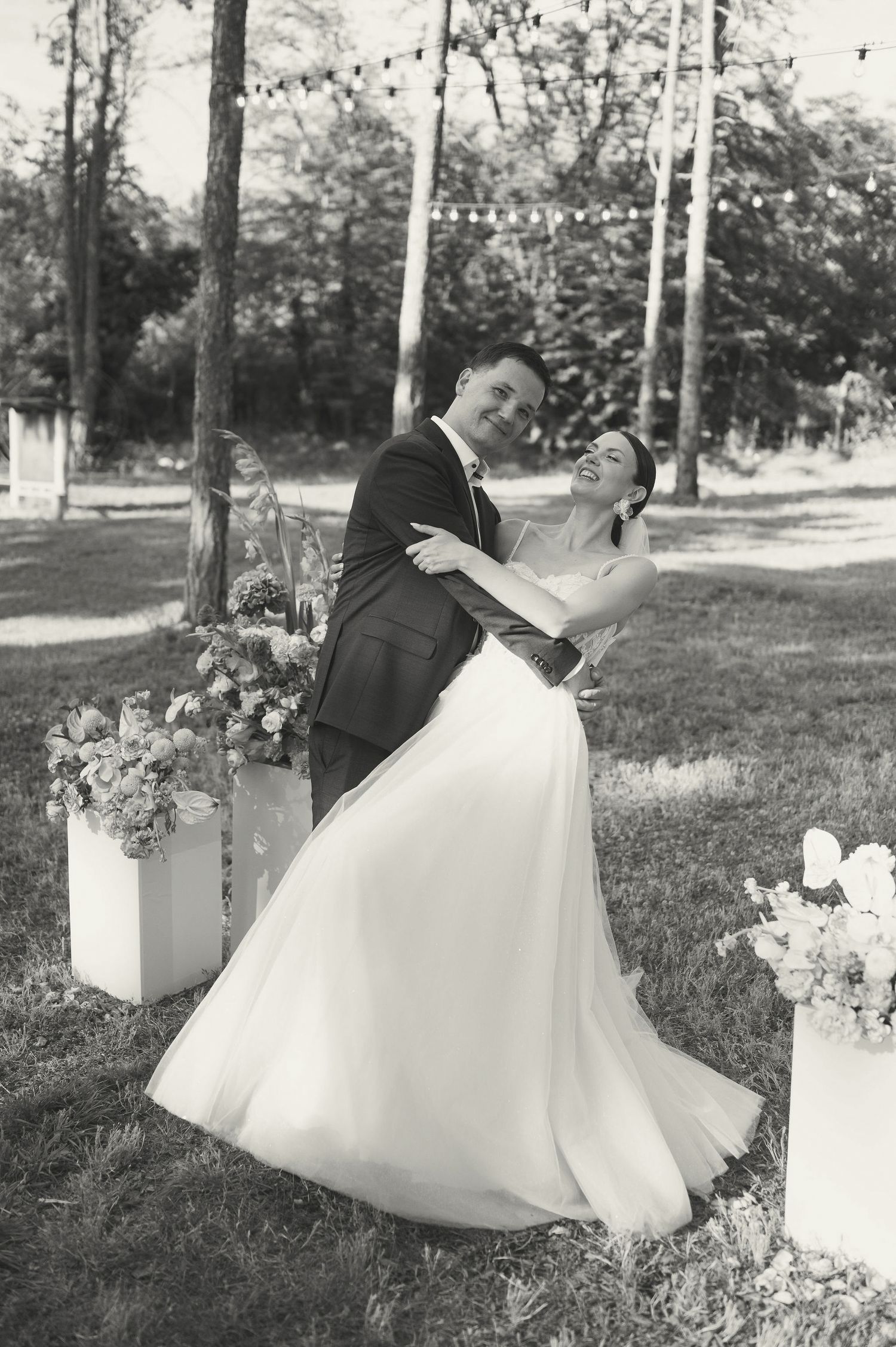 A dramatic black and white wedding photo showing a romantic dip pose under string lights.