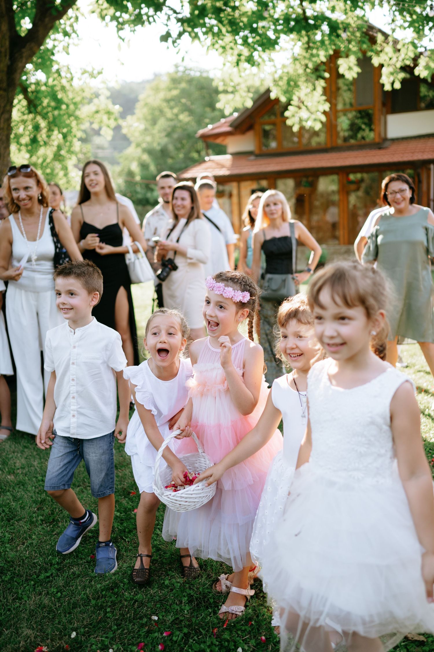 Joyful children and wedding guests gathered on a lawn during an outdoor celebration.