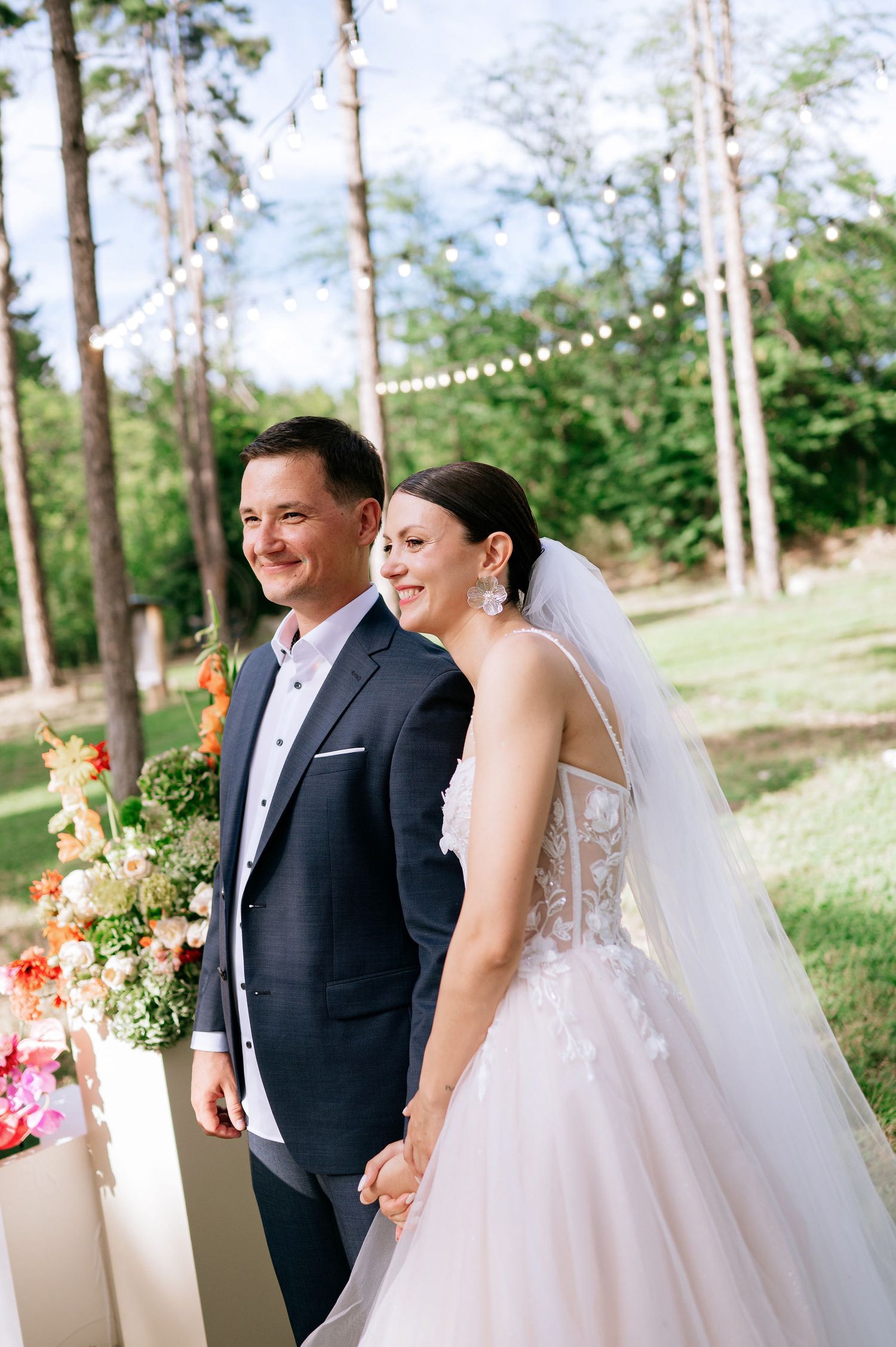 Candid wedding moment captured in a forest setting with string lights and floral decor.