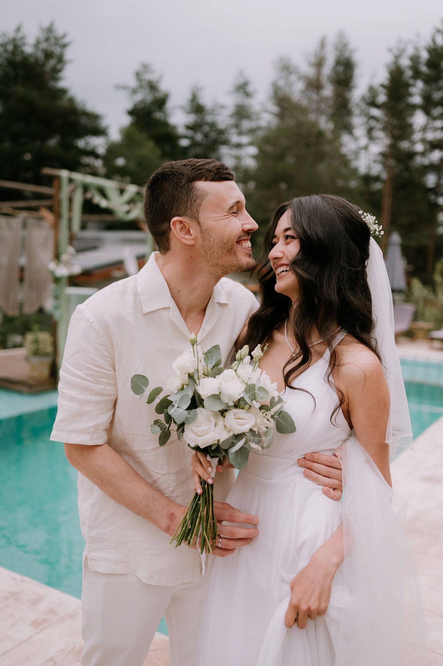 Couple in white shares joyful moments during their poolside wedding celebration.