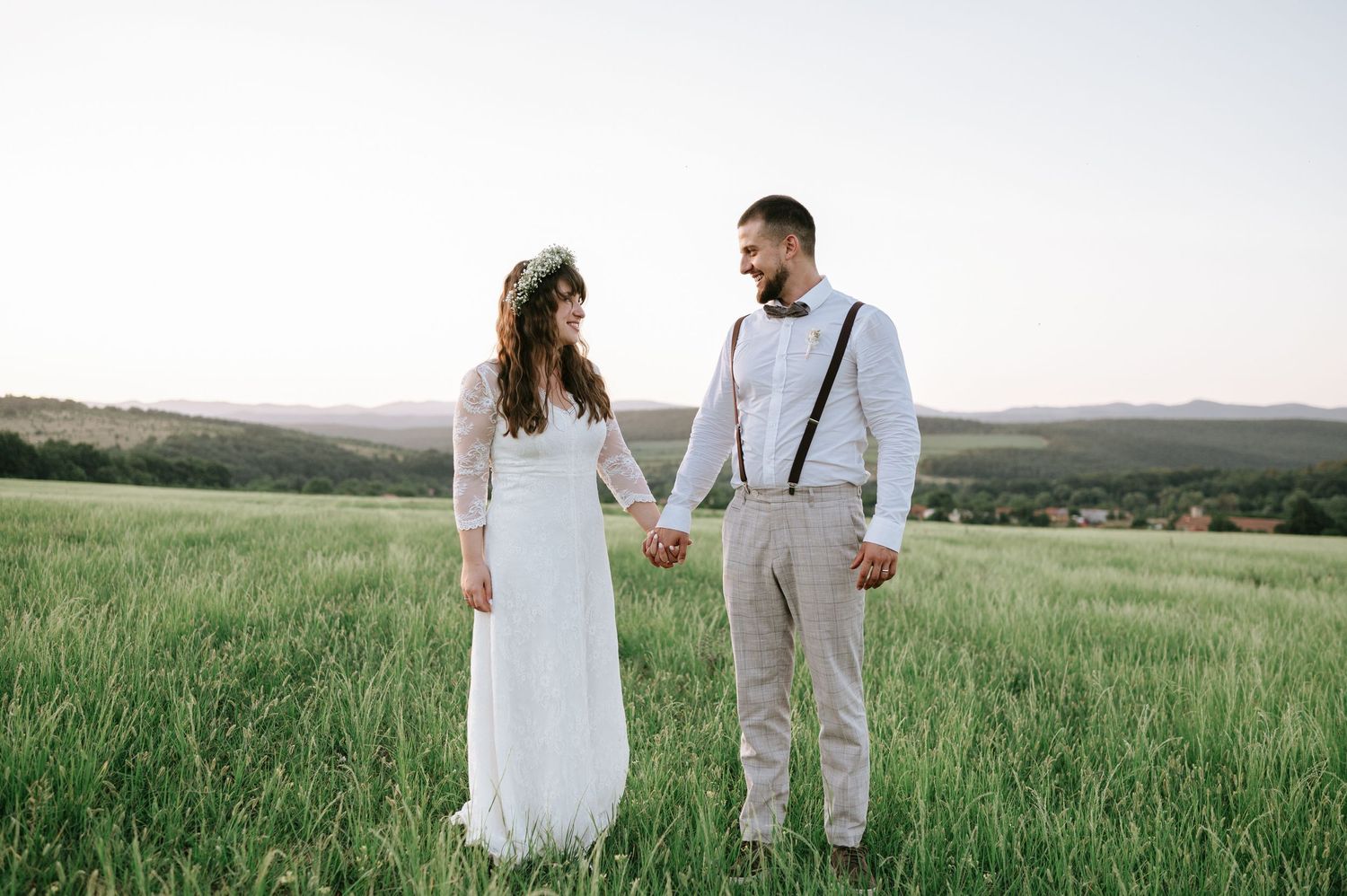 Couple in wedding attire standing together in a vast green field during golden hour.
