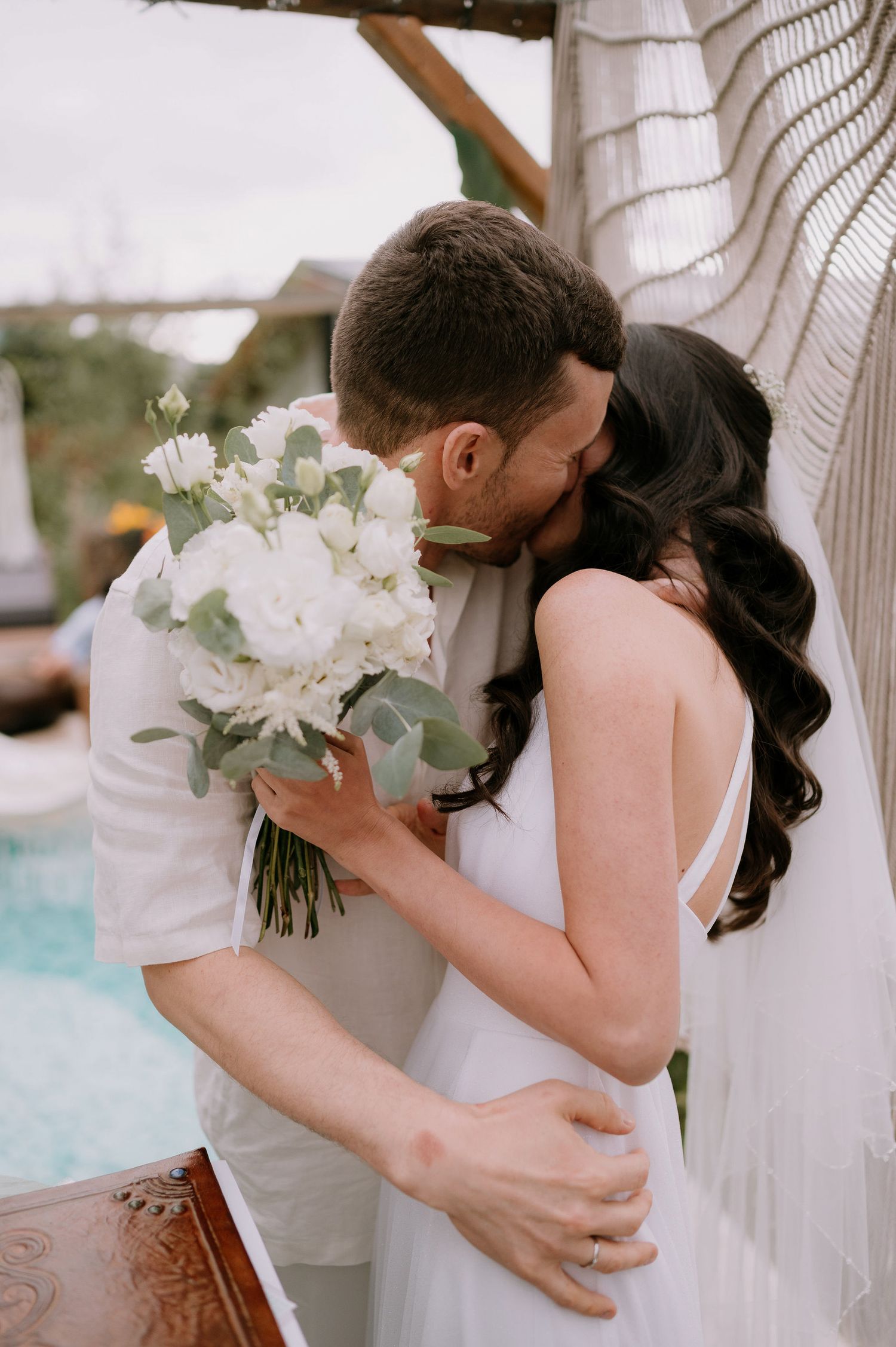Tender wedding embrace captured poolside with white floral arrangements.