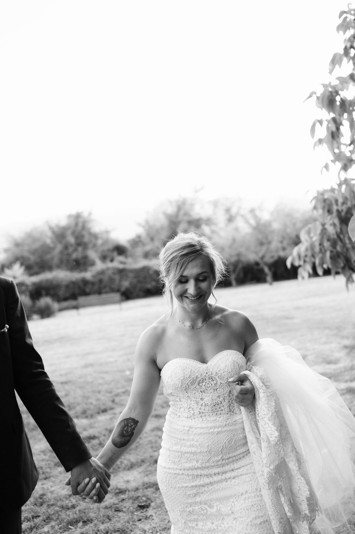 A bride in a beaded white gown walks across an outdoor field.