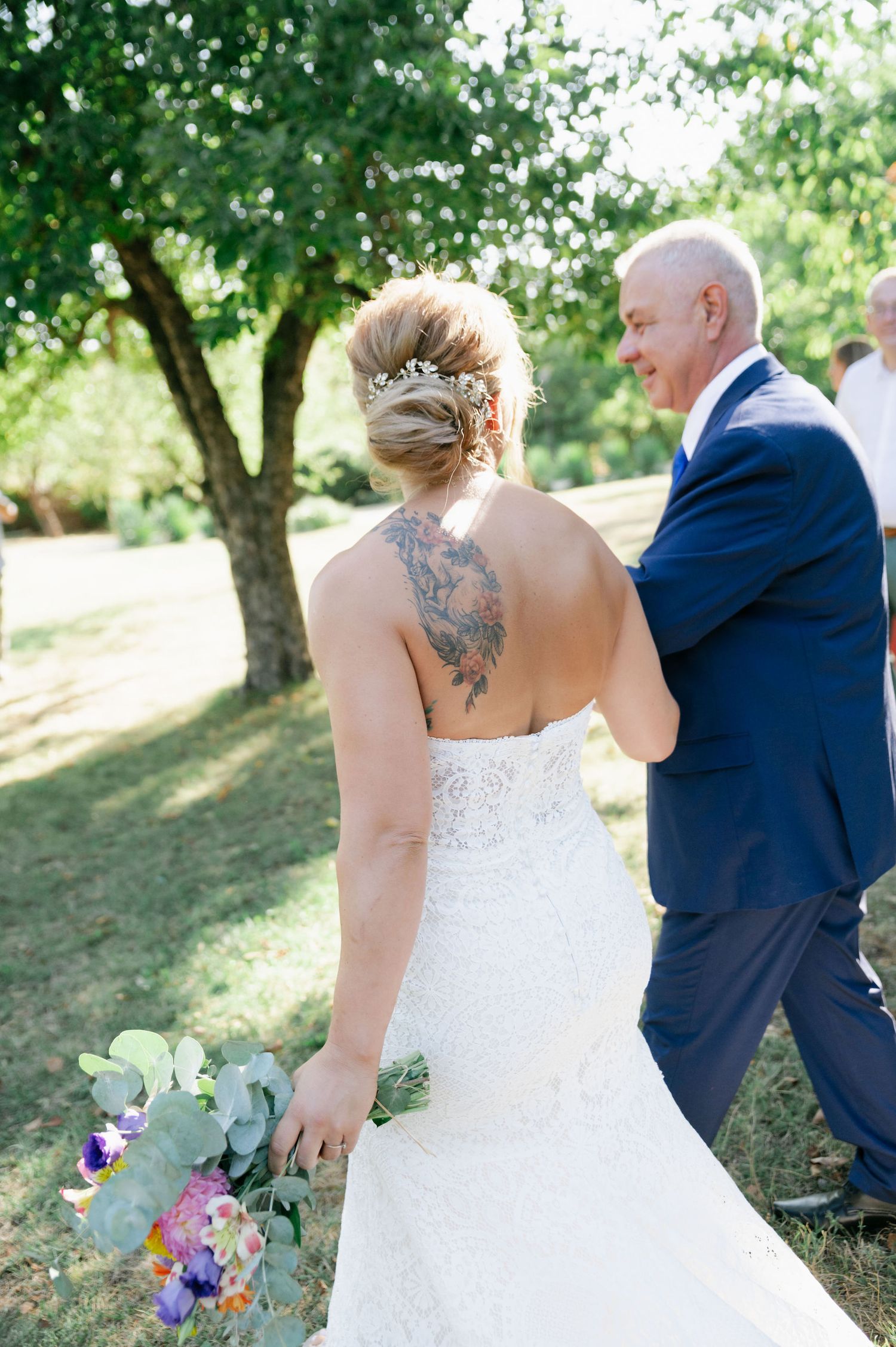 Bride carrying colorful bouquet walks with wedding party member through garden setting.