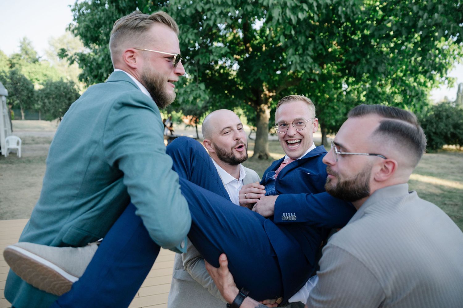 A group of people in formal wear engaged in a lighthearted group hug outdoors.