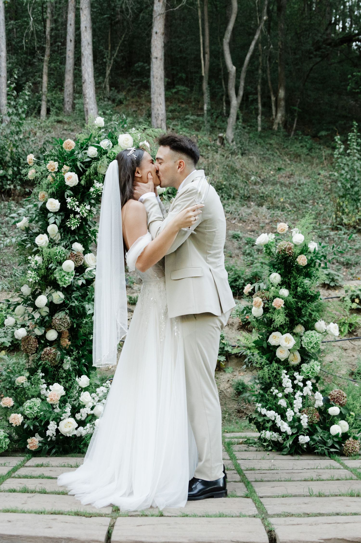 Romantic wedding moment captured on stone steps decorated with white roses in a forest setting.