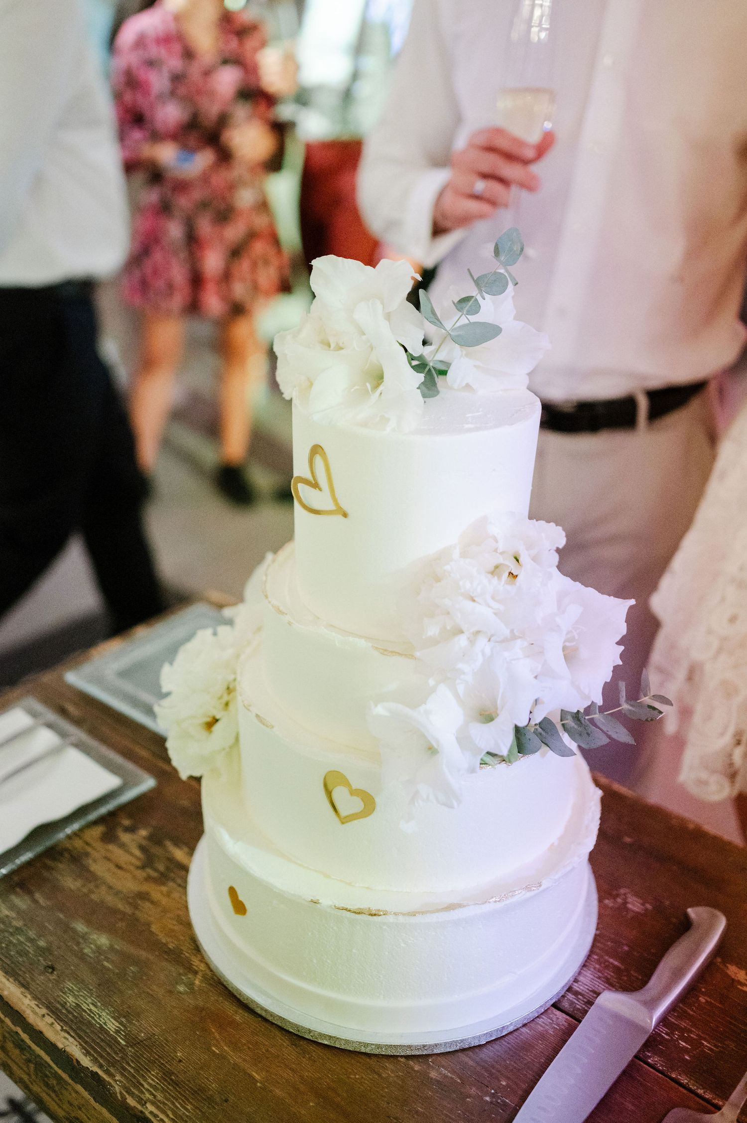 Elegant white wedding cake with delicate floral details displayed on rustic wooden table.