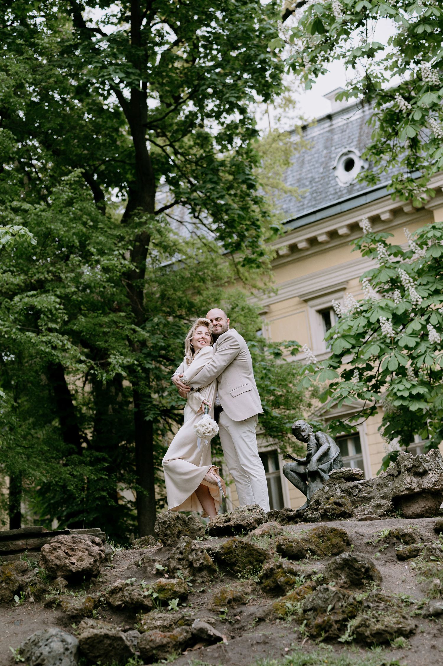 A romantic couple poses on rocky terrain with a historic building visible in background.