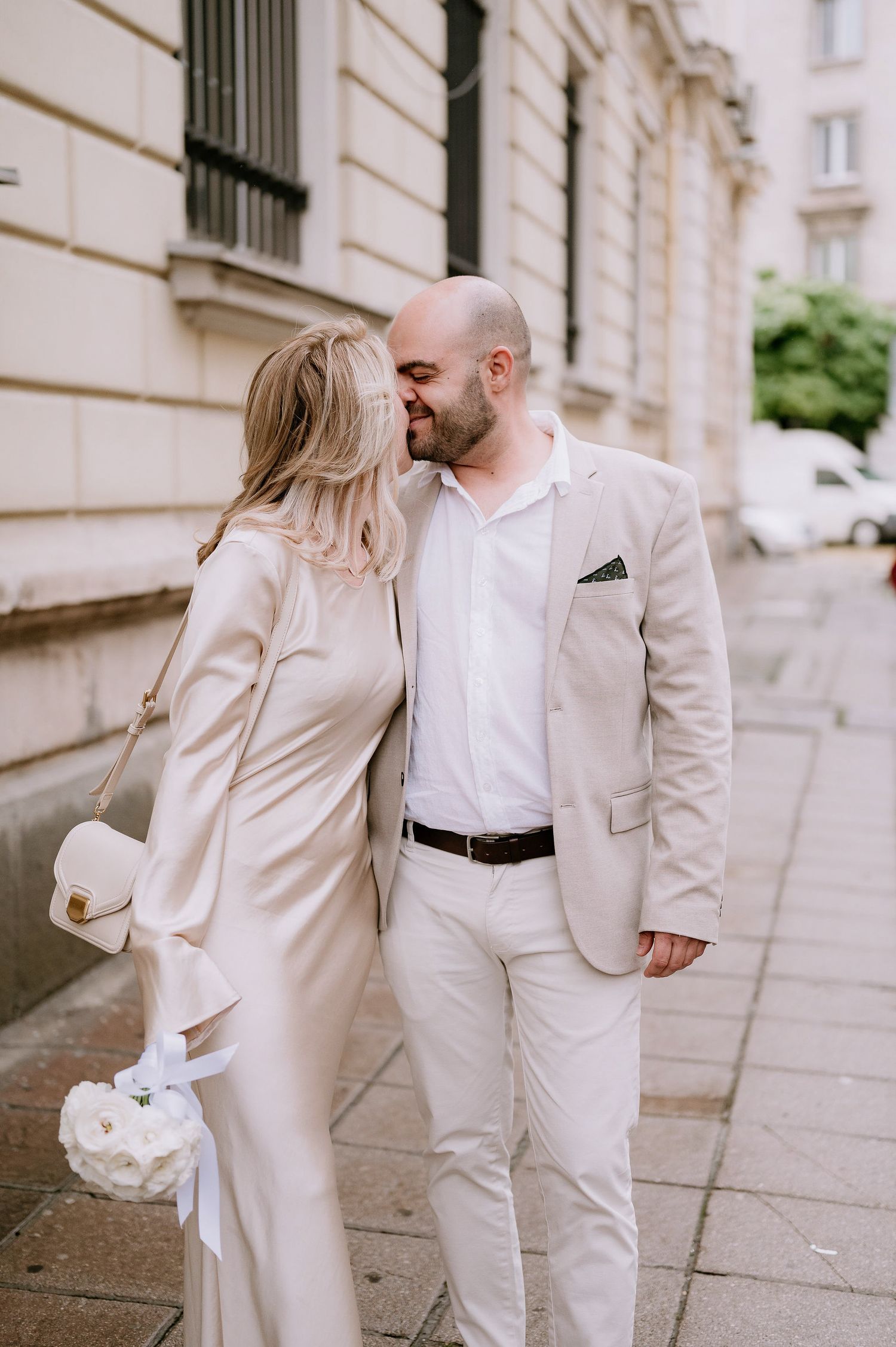 Romantic moment between couple dressed in cream colored outfits on a European street.