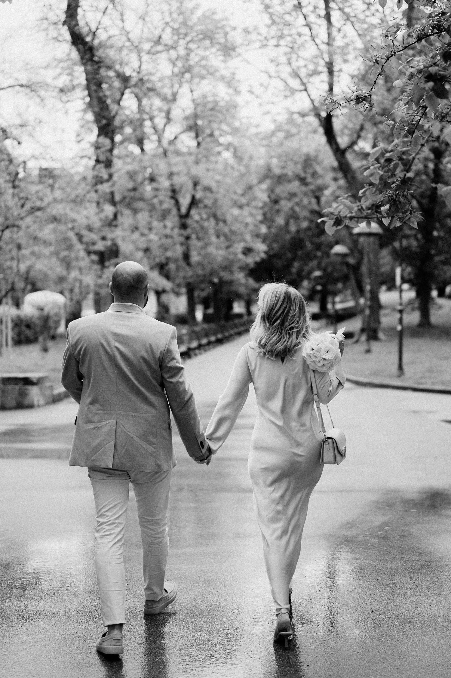 Black and white image of a couple strolling together on a rain-soaked path.