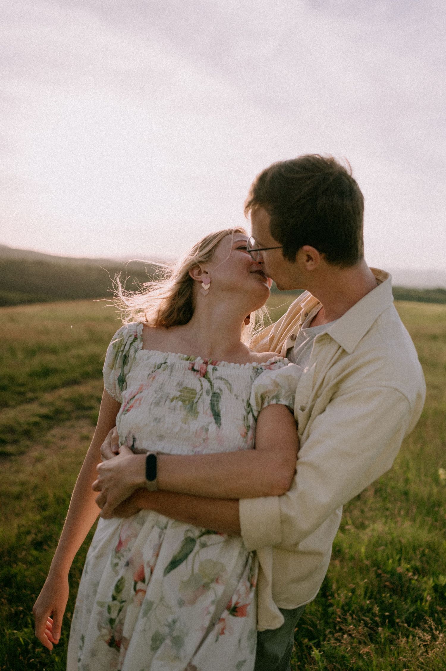 Romantic couple embracing in a sunlit field during sunset photoshoot.