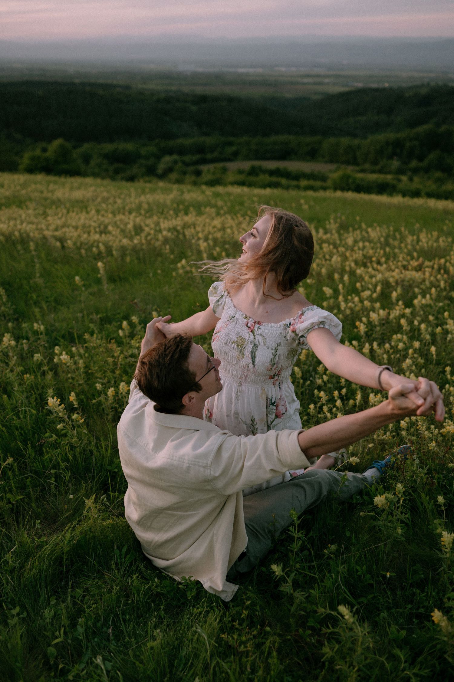 Two people dance playfully together in a wildflower meadow at dusk.