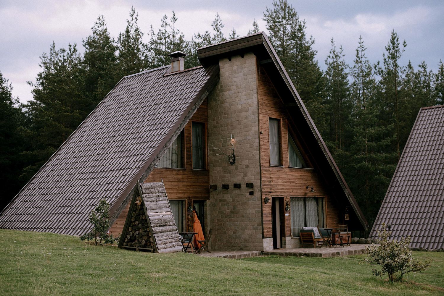 A-frame wooden cabin with stone accents surrounded by tall pine trees.