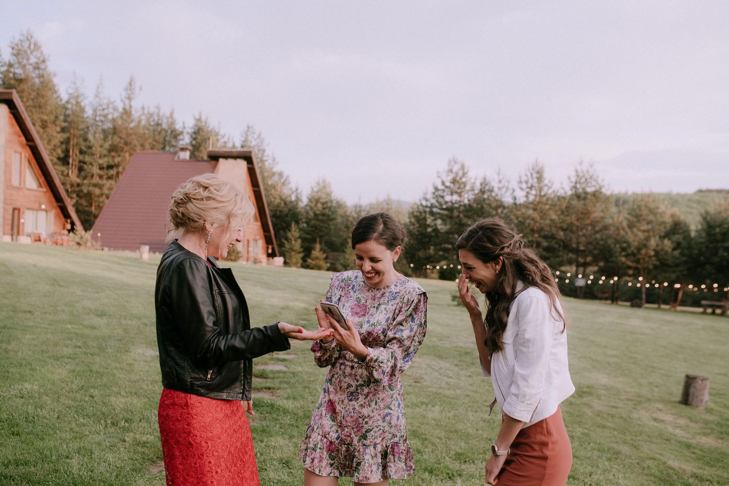 A group dances and celebrates outdoors on a grassy hill during a sunset gathering.