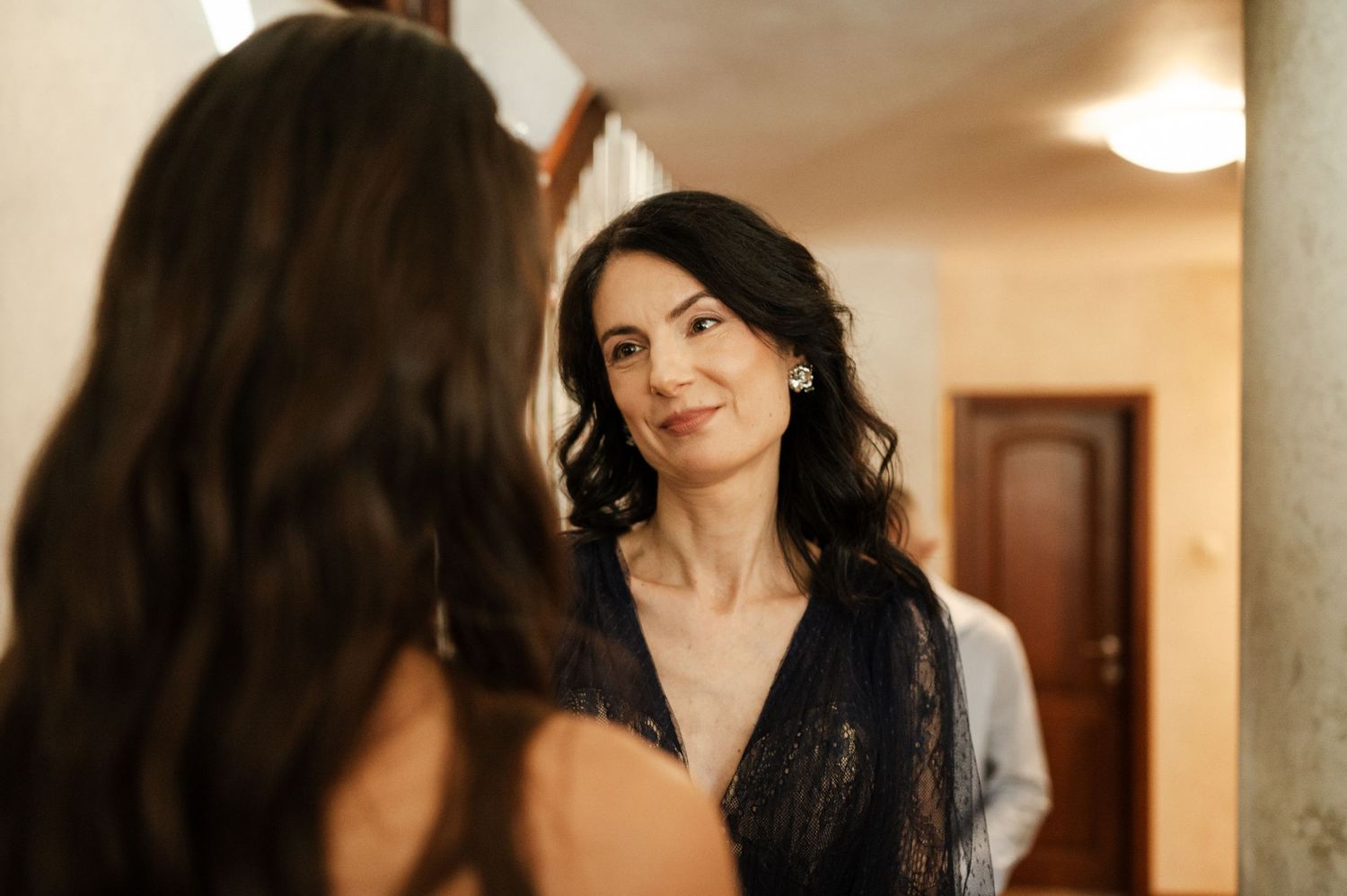 A person in formal attire poses elegantly near interior columns.