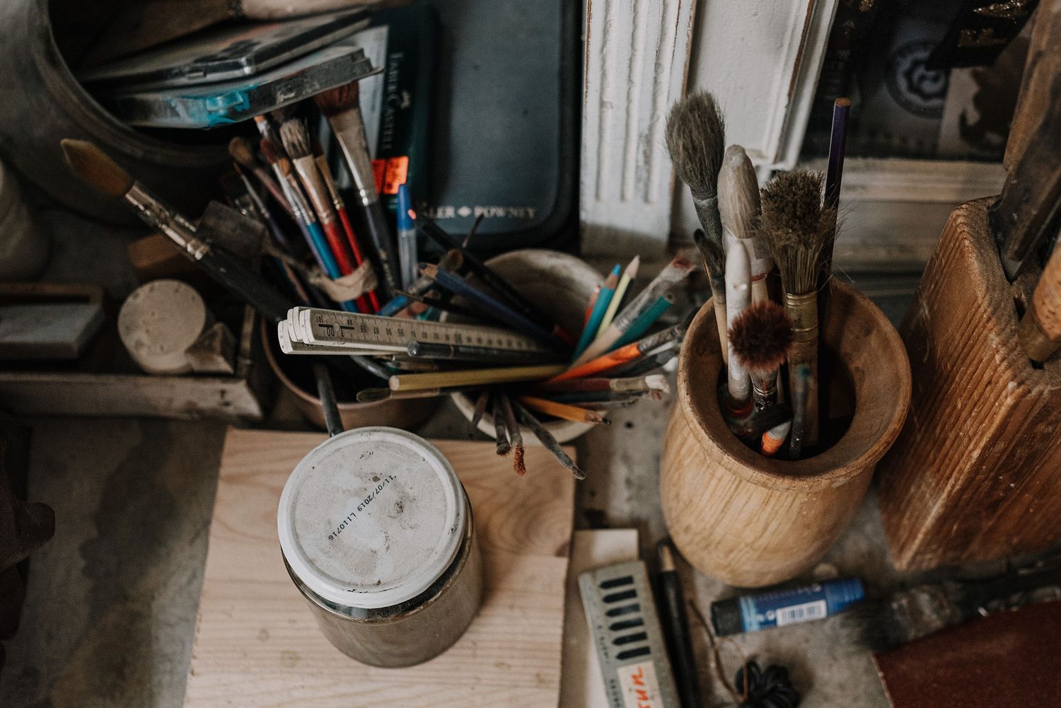 Collection of art supplies and tools arranged on a wooden work surface.