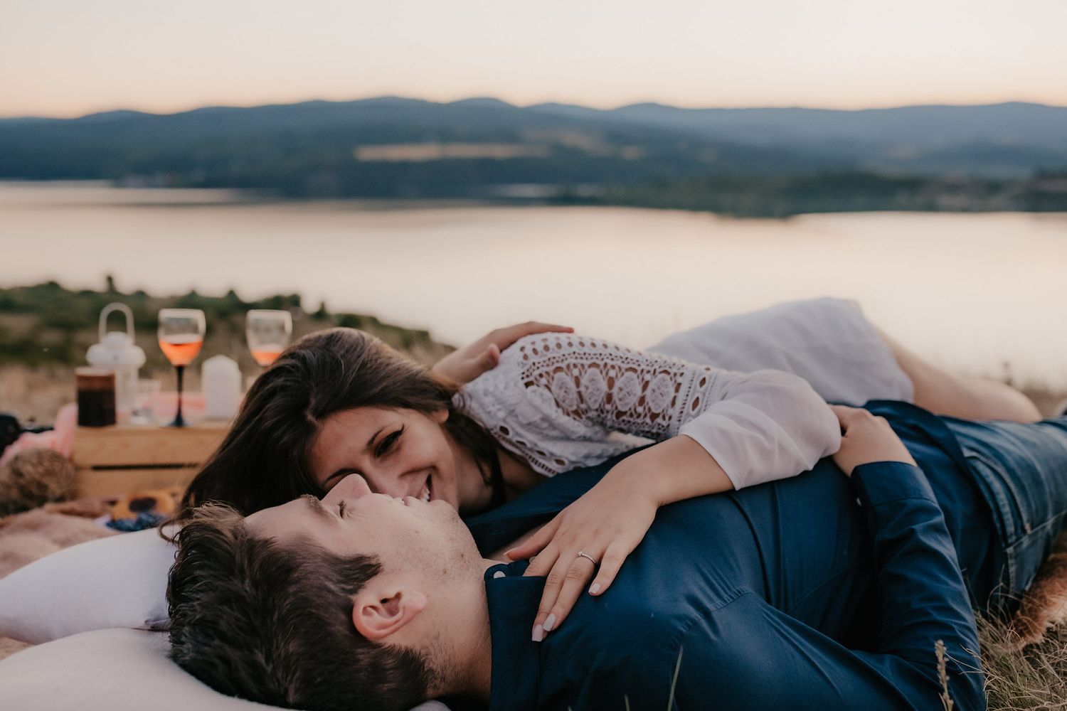Couple embracing on a rocky cliff overlooking a scenic mountain lake at sunset.