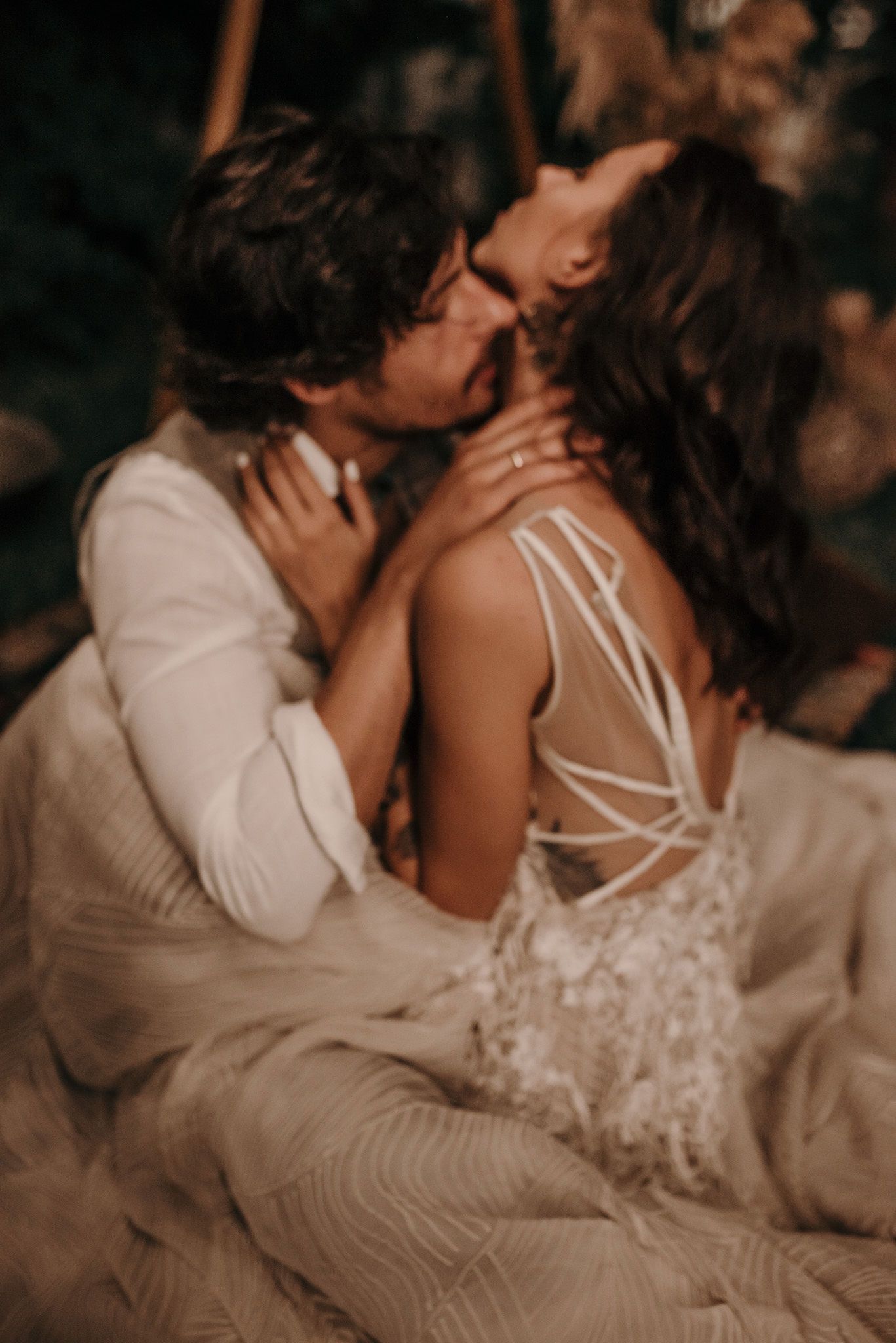 A romantic couple shares an intimate kiss in warm lighting while wearing wedding attire with a detailed lace back dress.