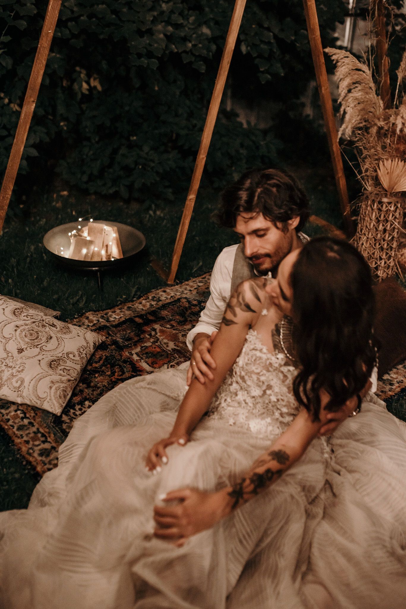 A romantic couple sits together in a bohemian tent setting with candlelight and decorative pillows.