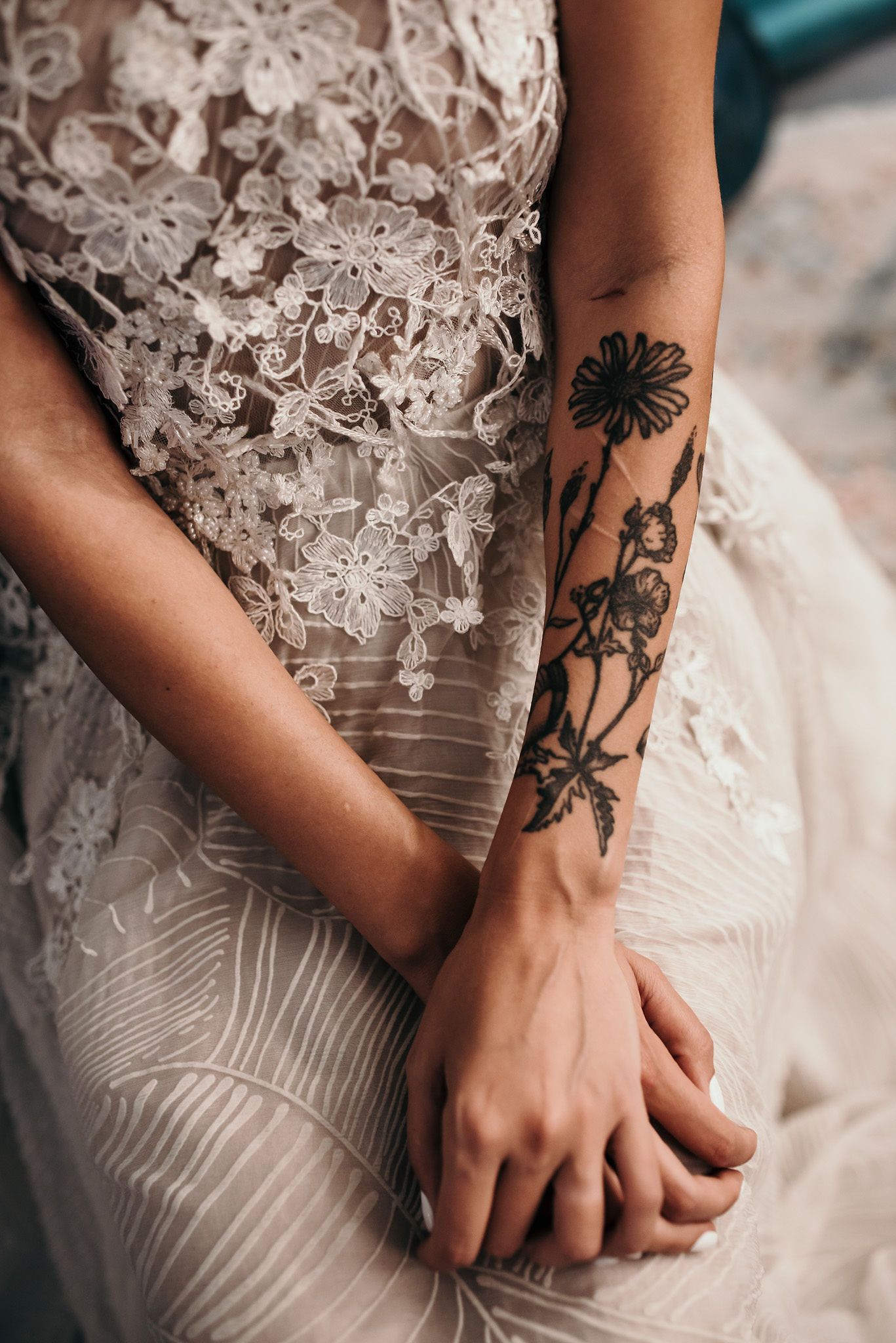 Detailed view of floral arm tattoos contrasting with white lace wedding dress details.