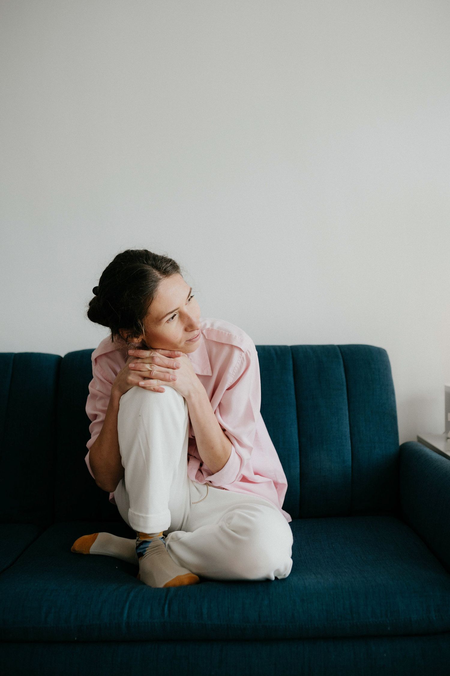 Person in pink sweater curled up on navy blue couch in minimalist setting with natural lighting.