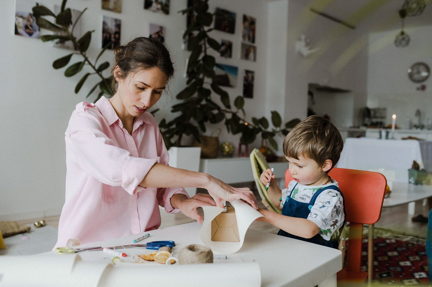 Two people sit at a white table working on a craft project together with plants and decor in the background.