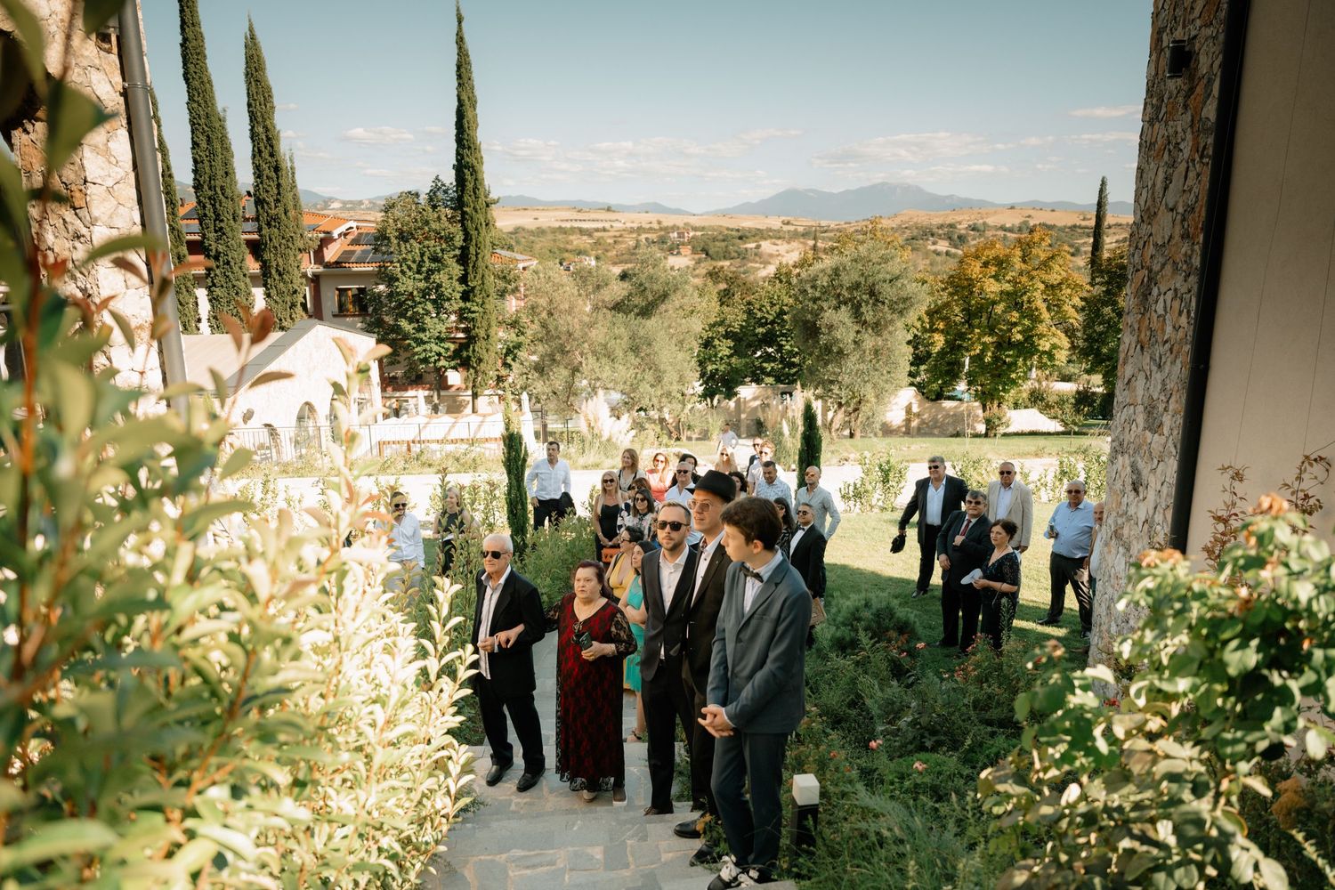 Outdoor wedding ceremony setup in a Tuscan garden with tall cypress trees and mountain views in the background.