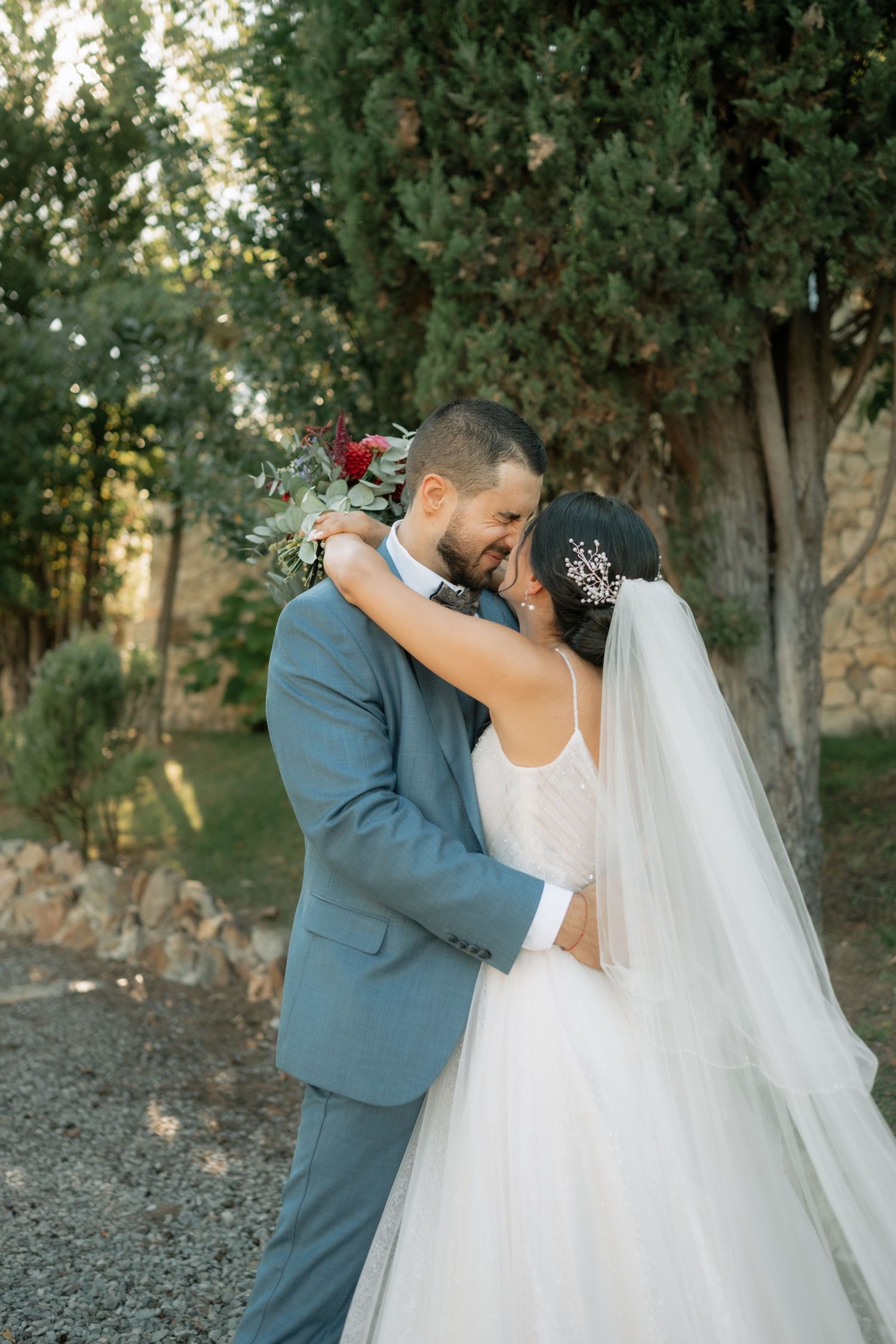Romantic wedding couple embraces outdoors in a natural wooded setting with soft evening light.