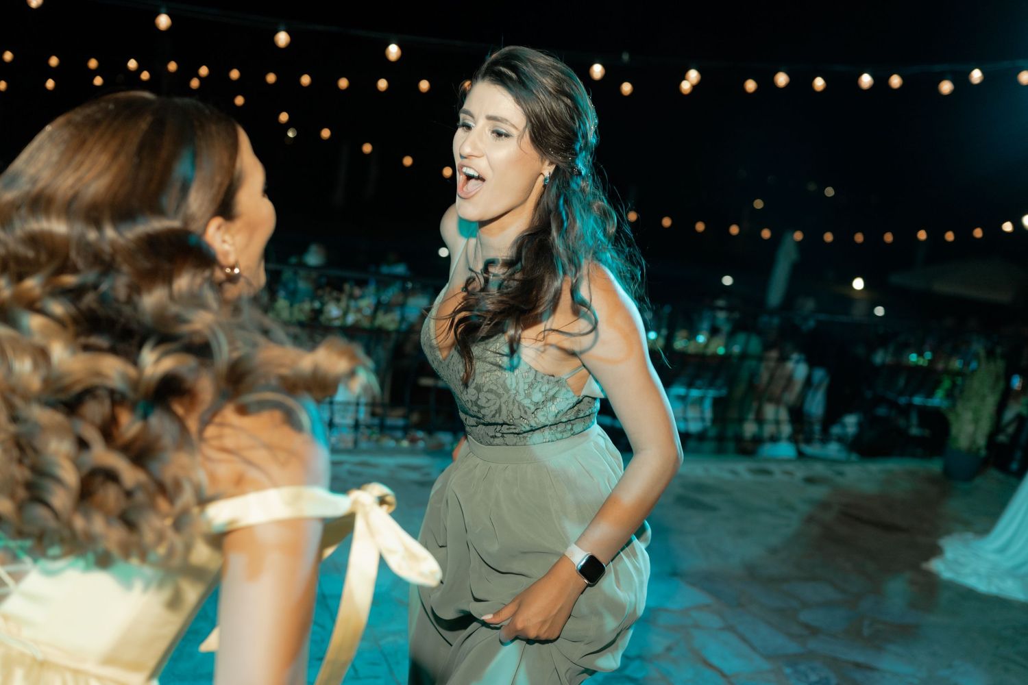 A couple dances together on an outdoor dance floor at night under twinkling string lights.
