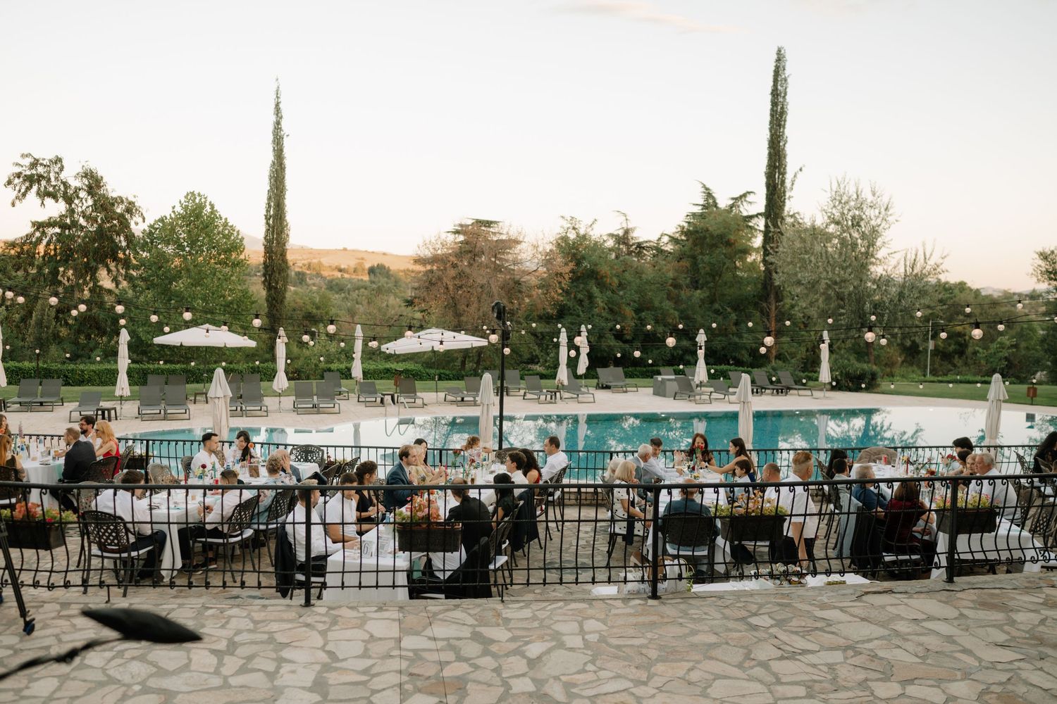 A panoramic view of a swimming pool area with lounge chairs and umbrellas at sunset.