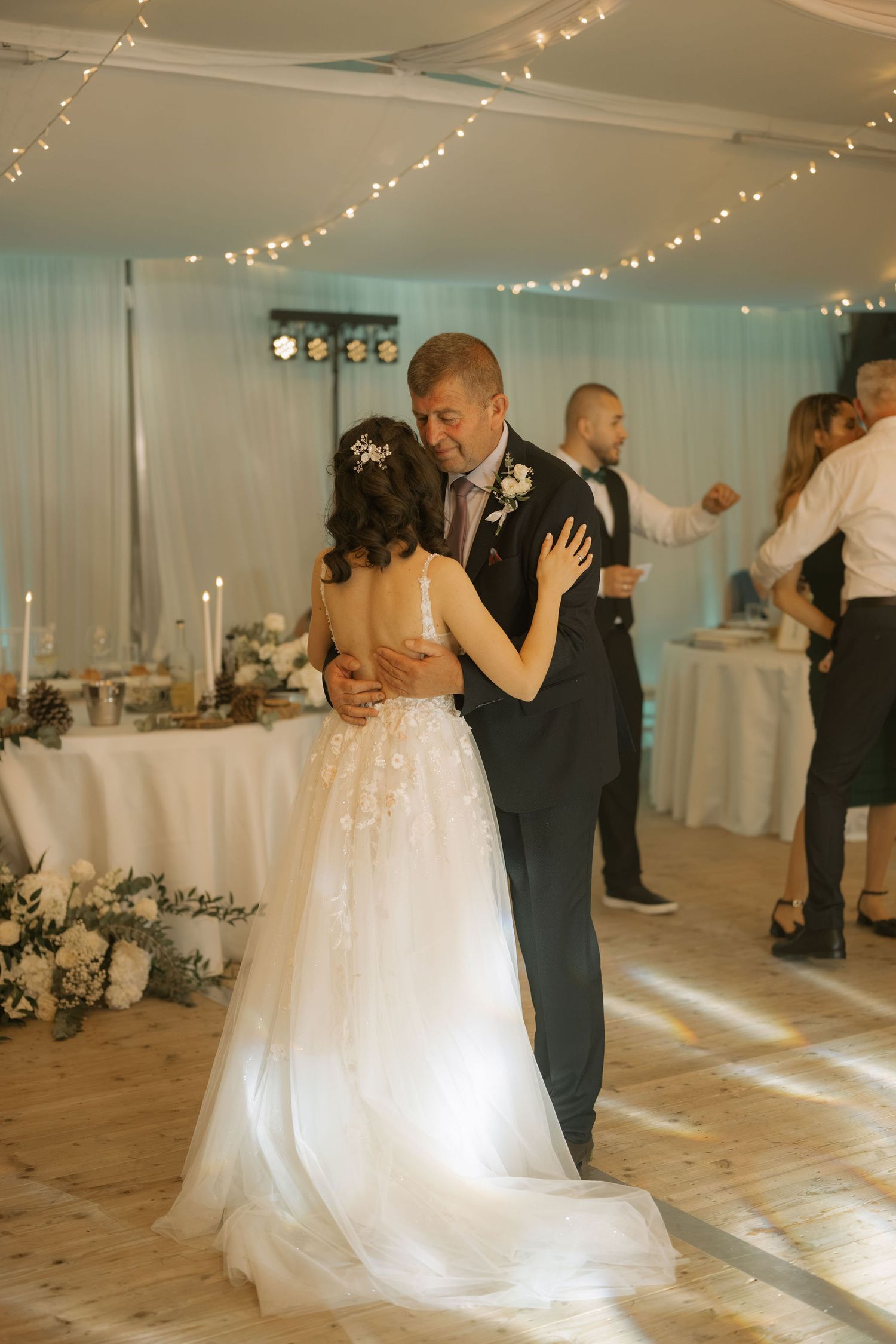 Bride and groom share their first dance at elegant wedding reception with fairy lights and floral decorations.