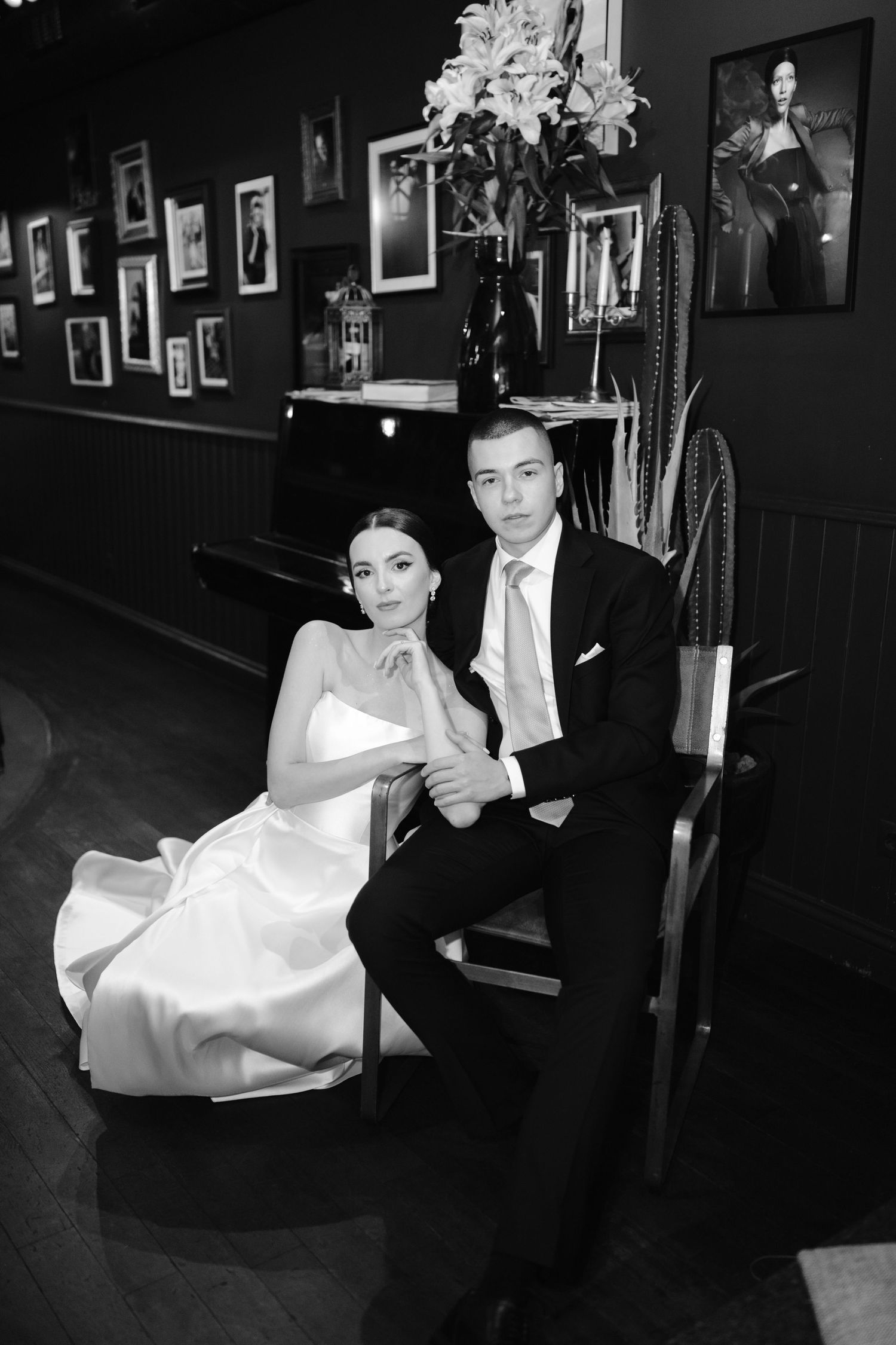 A couple in formal attire dance together in a dimly lit venue with framed photos on the wall.
