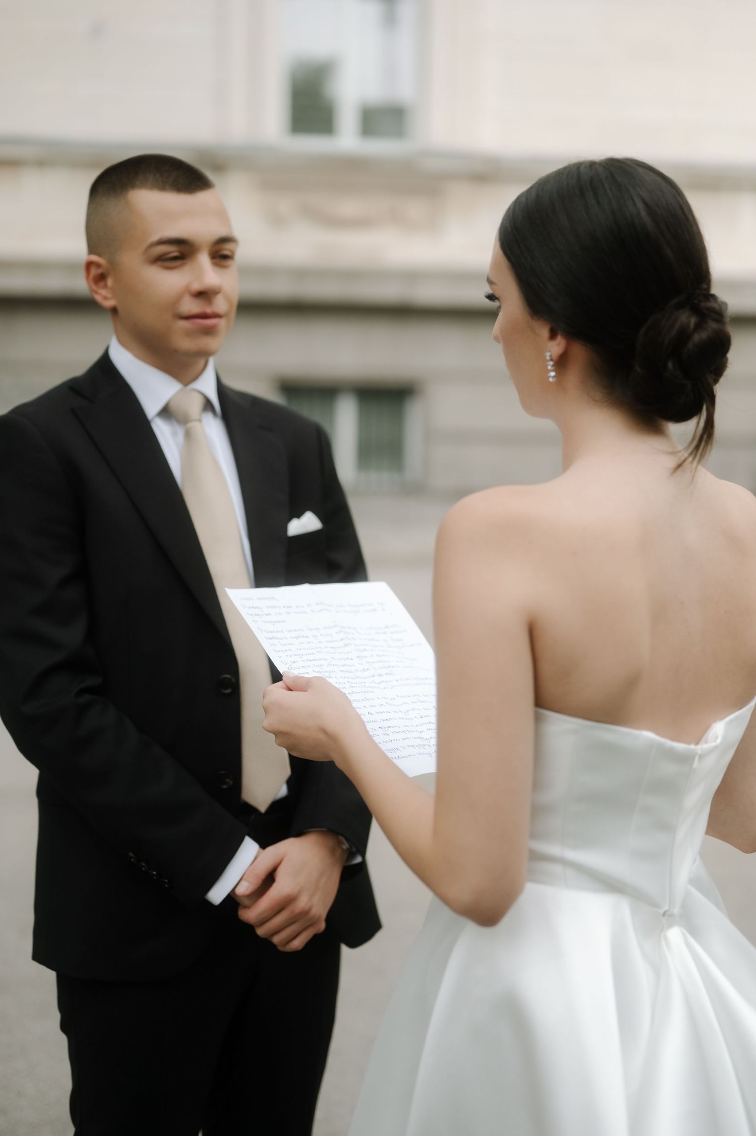 A couple exchanges vows during their wedding ceremony, with the bride in a white gown and groom in a black suit.