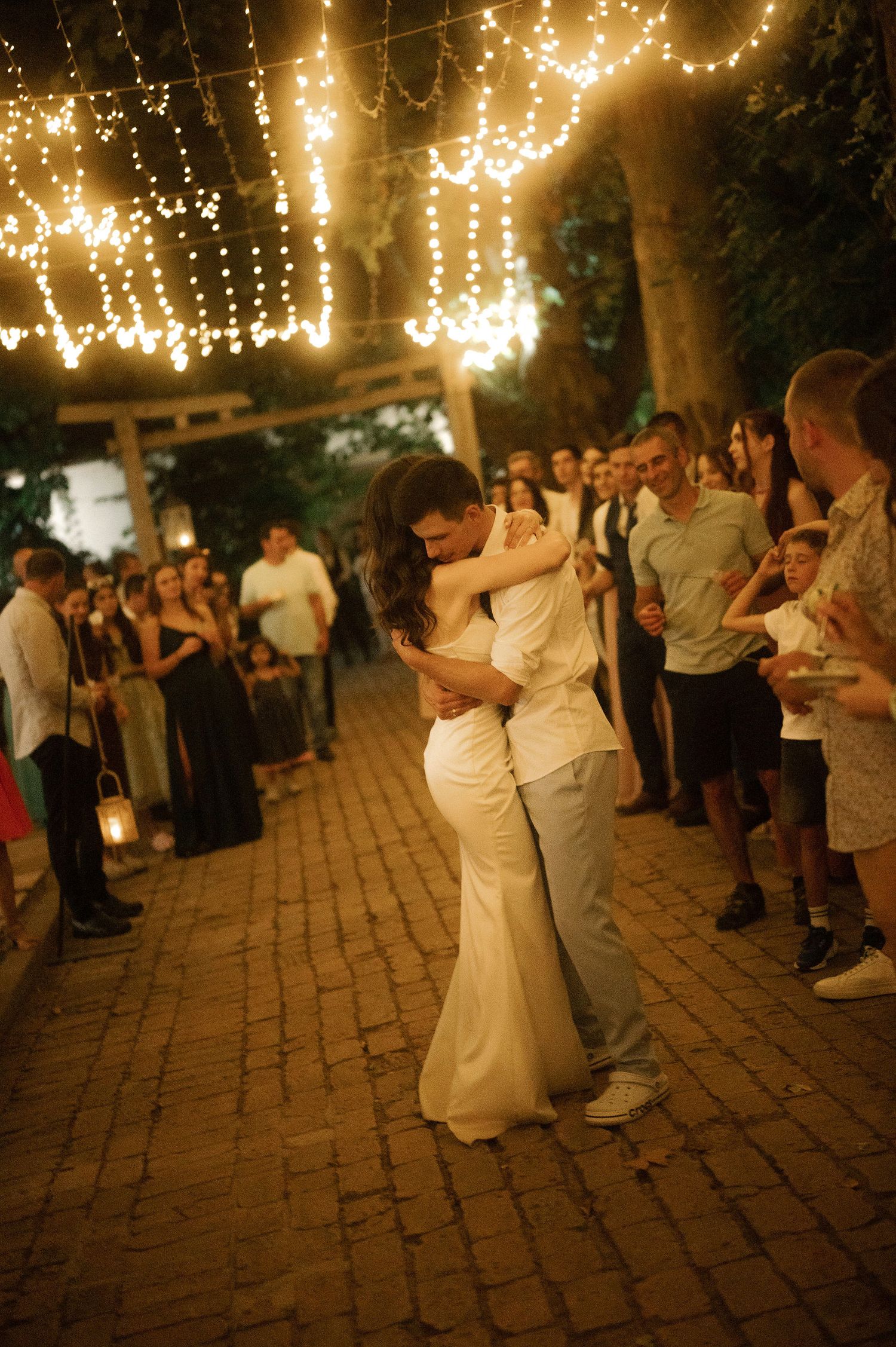 Couples dance under romantic string lights at an outdoor evening wedding reception on a brick patio.