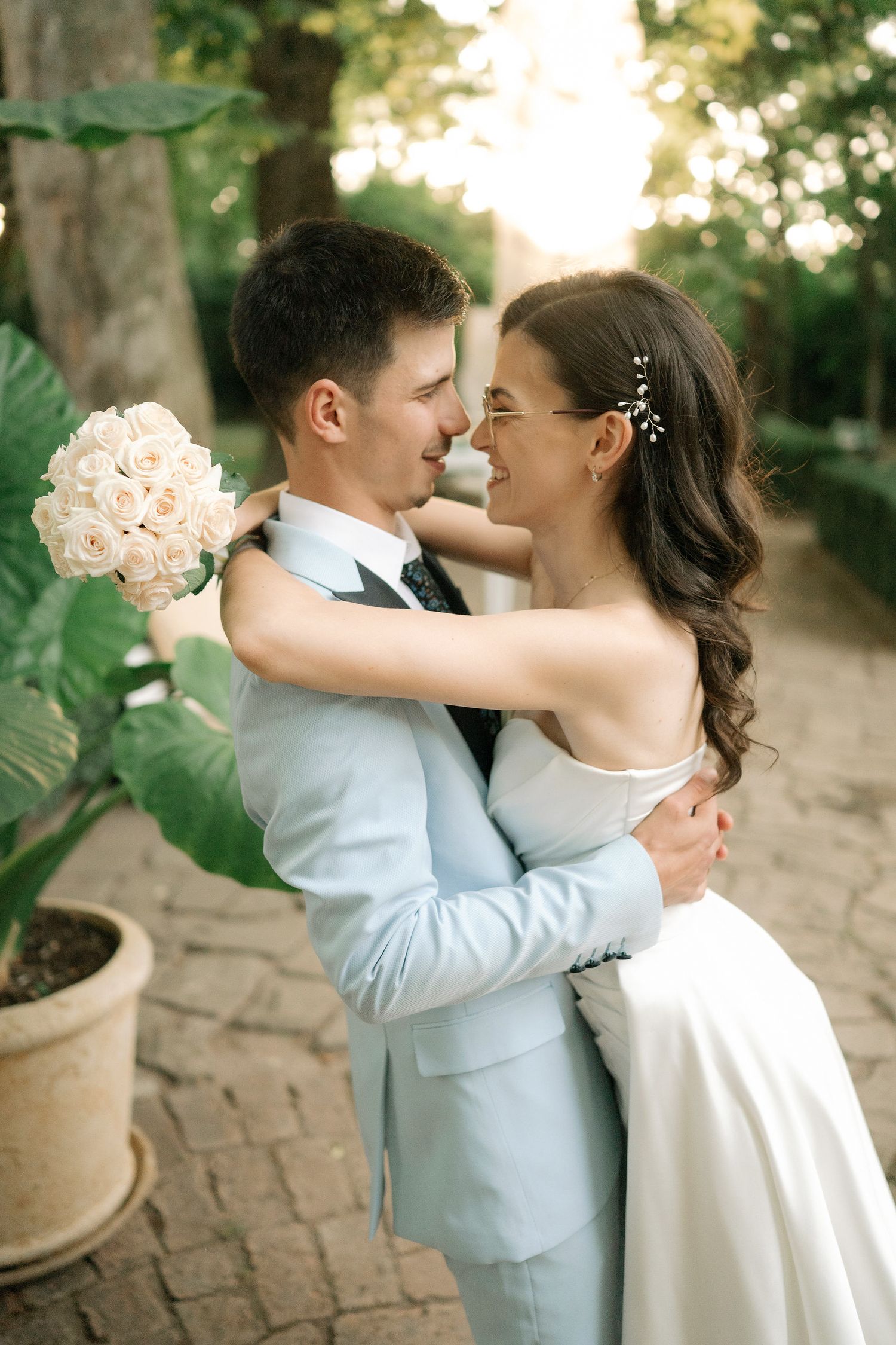 A romantic wedding couple shares tender moments in a garden setting wearing light blue suit and white dress.