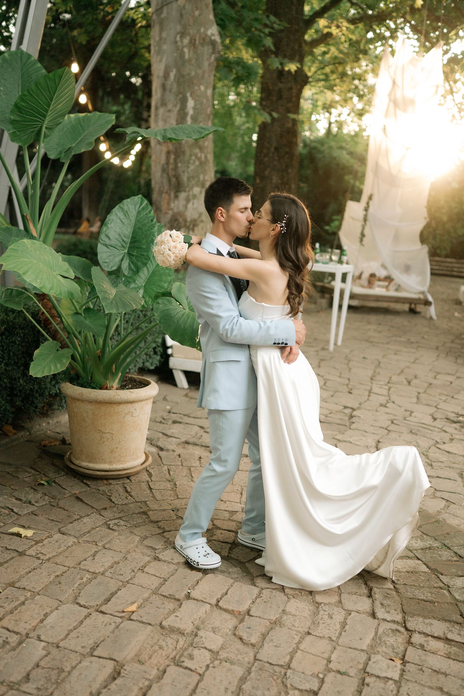 A romantic couple shares an intimate dance moment on a stone patio surrounded by greenery at sunset.