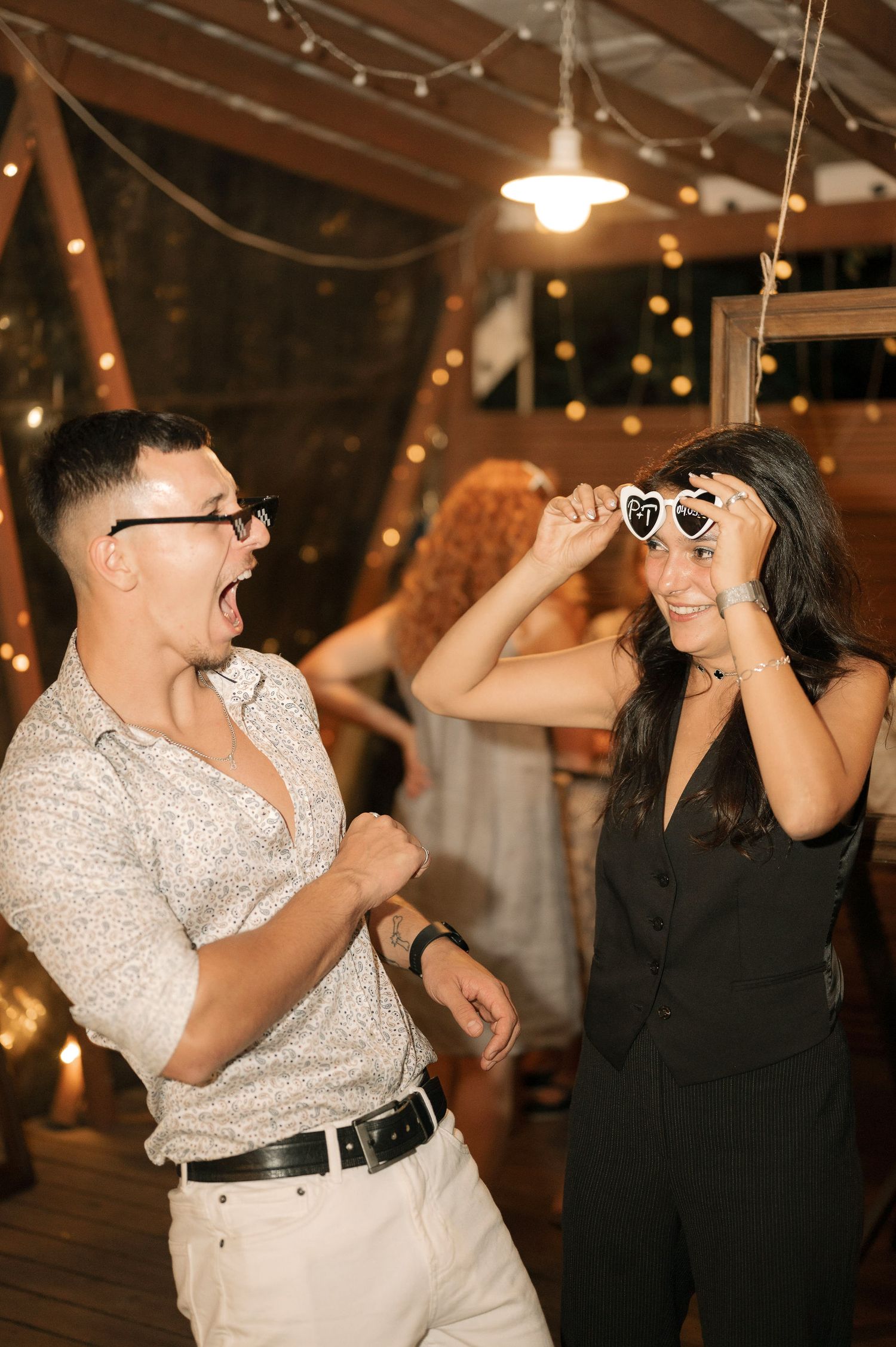Two people share a fun candid moment dancing together at an indoor venue with warm lighting and festive decor.