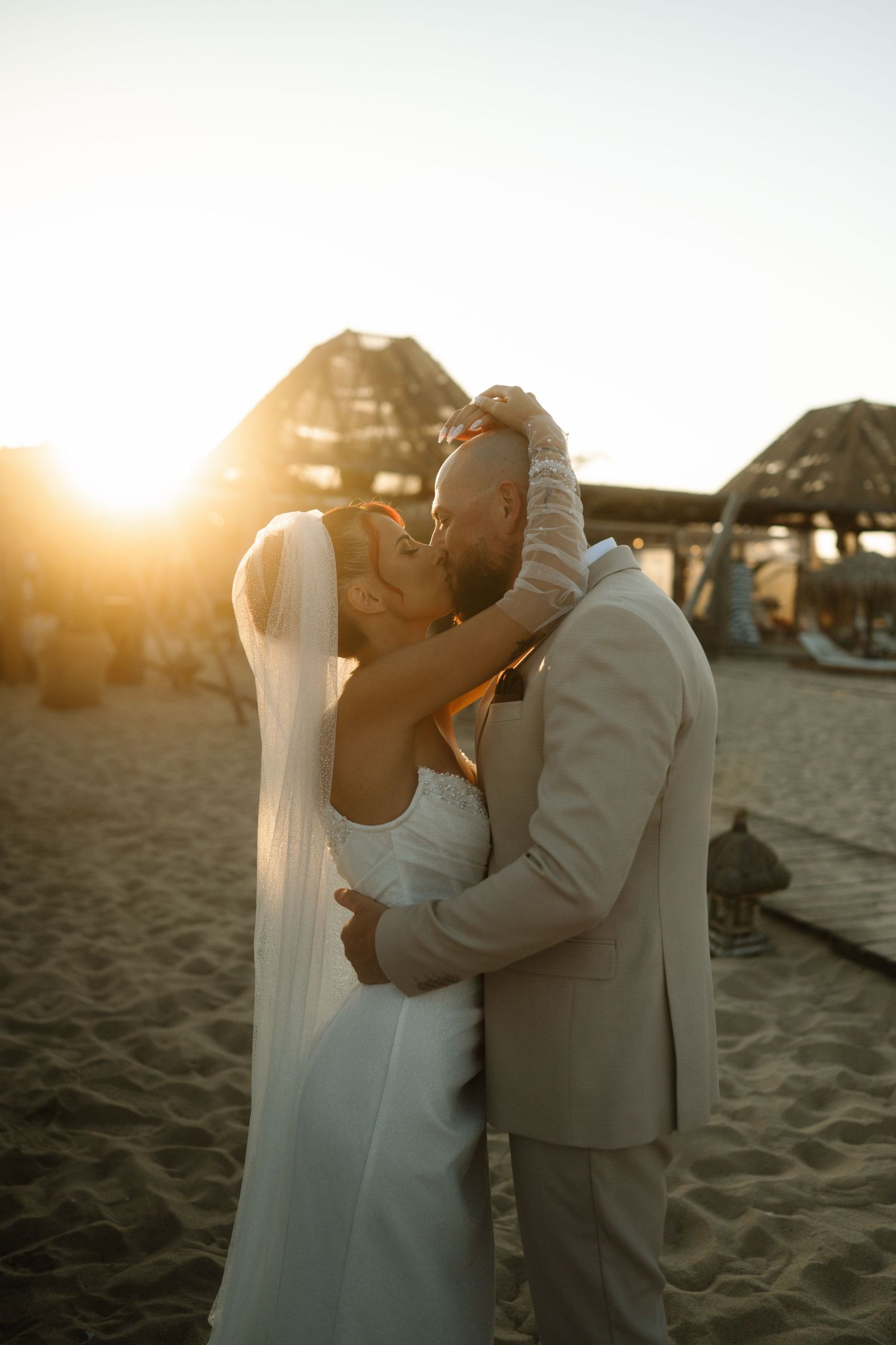 A romantic beach wedding moment captured at sunset with a couple embracing against a golden sky.