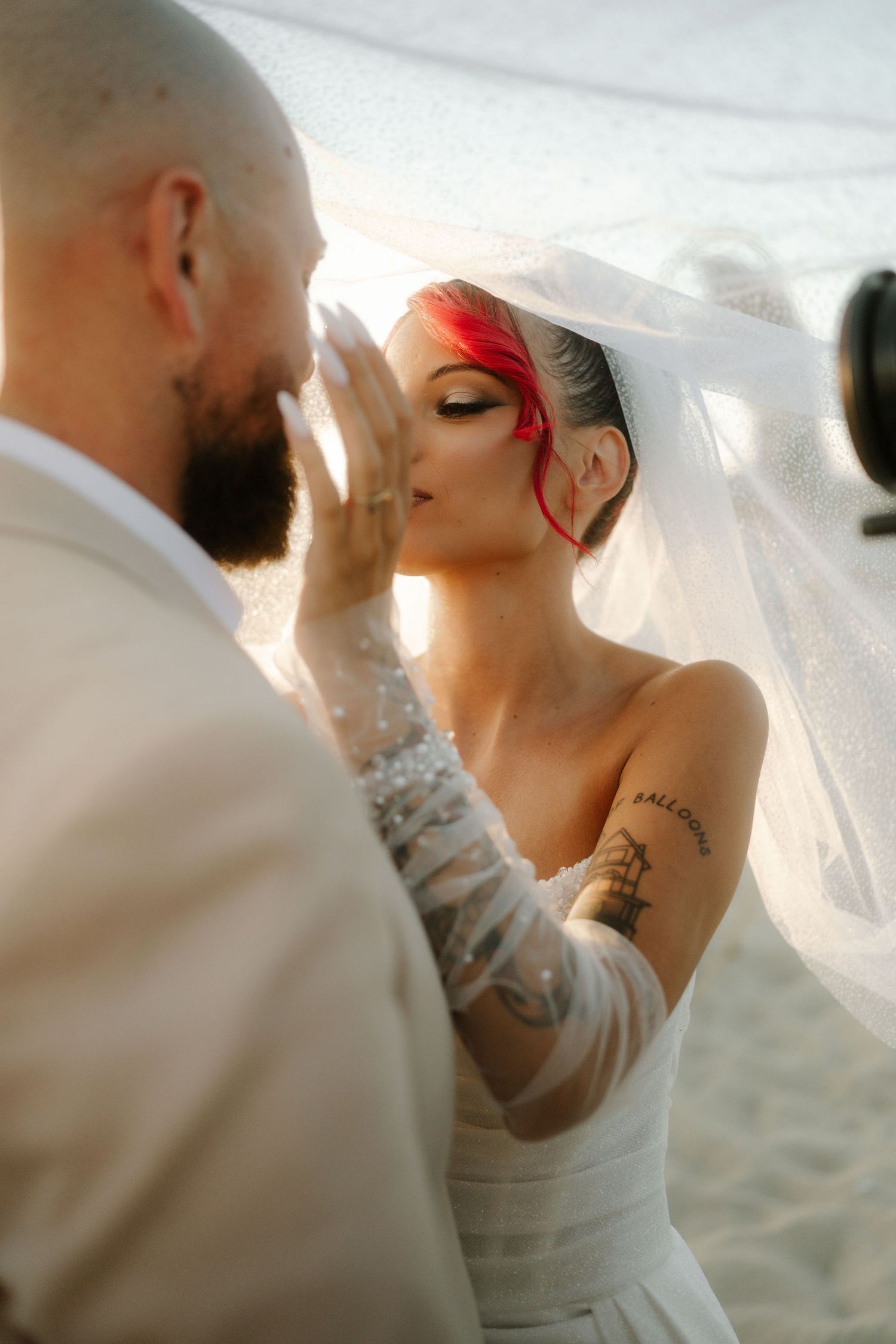 A romantic wedding couple shares an intimate moment under a veil during a sunset beach ceremony.