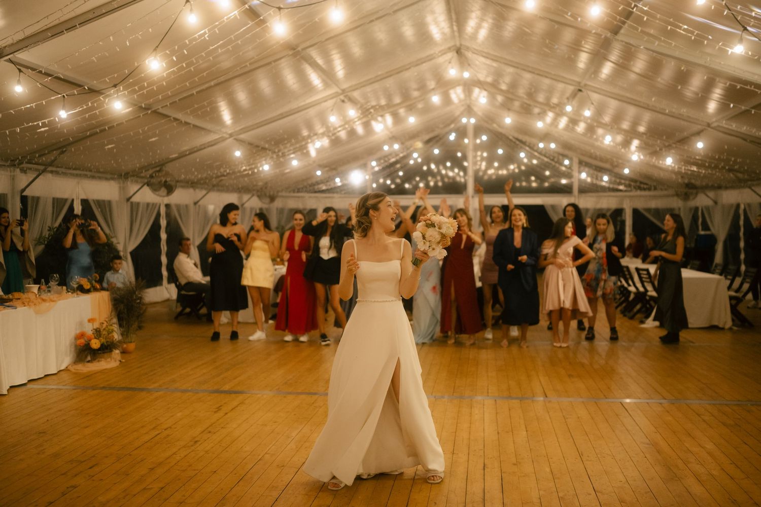 A wedding reception in a tent venue with string lights overhead and a wooden dance floor.