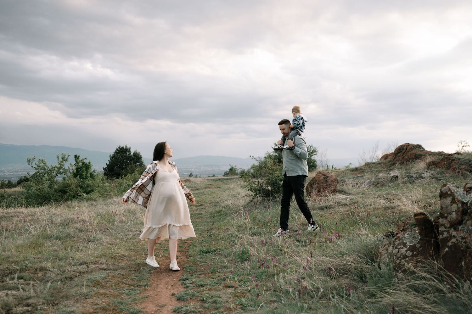 A couple walks along a scenic hillside path under moody cloudy skies during an outdoor photo session.