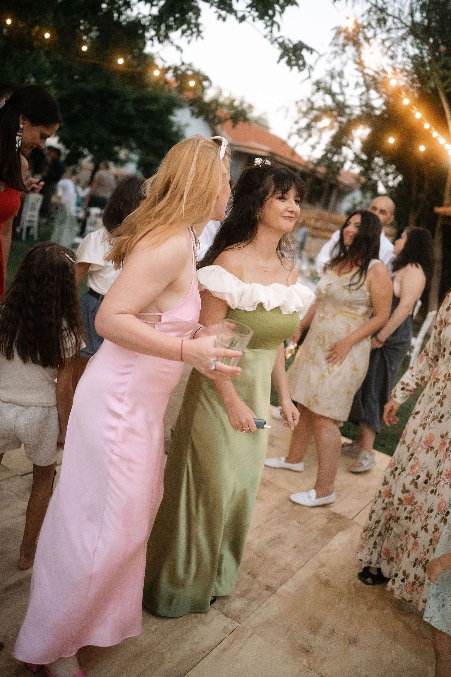 A group celebrates at an outdoor party with string lights and casual summer attire.