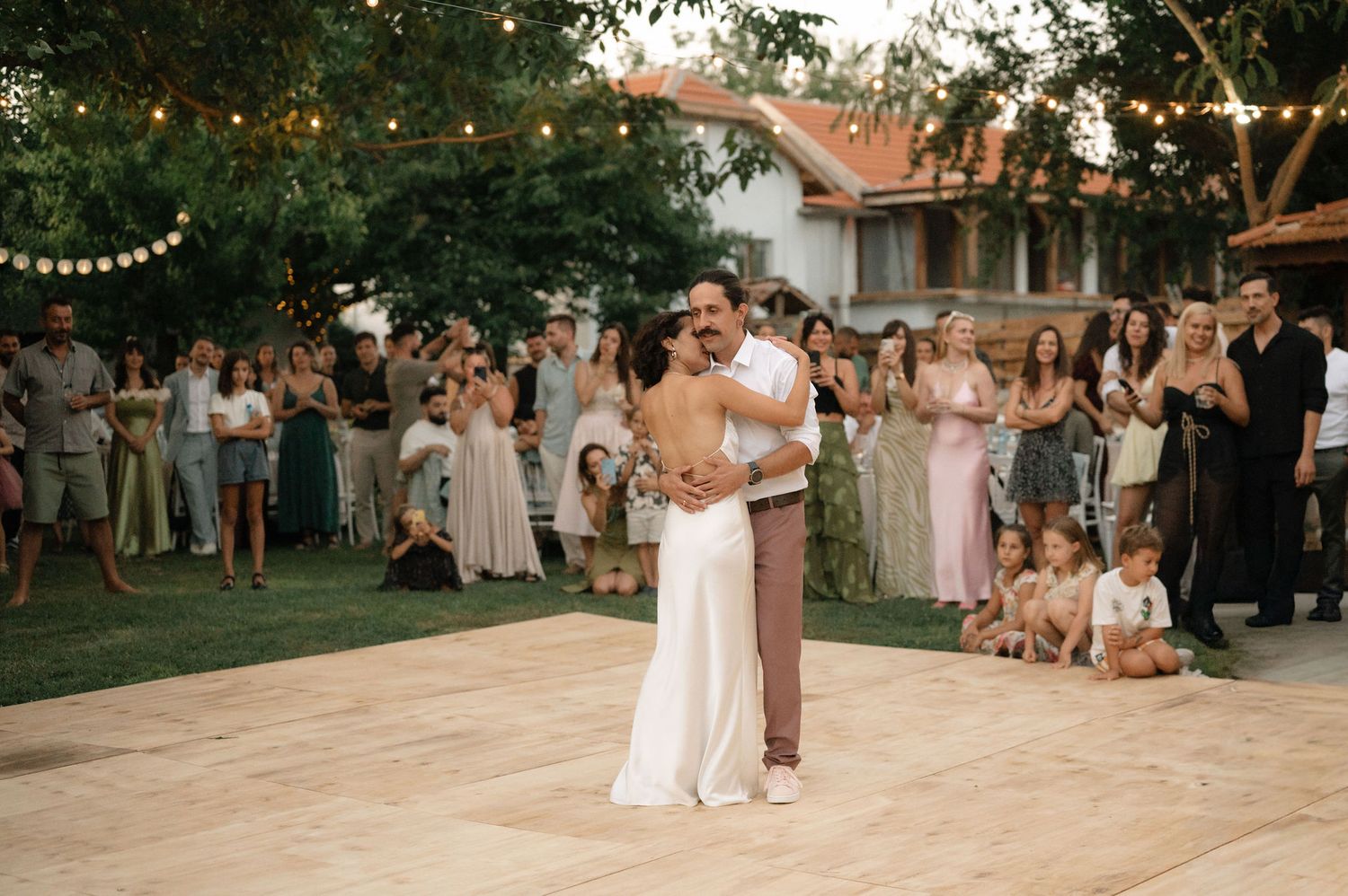 Wedding guests dance together on an outdoor patio during a sunset reception celebration.