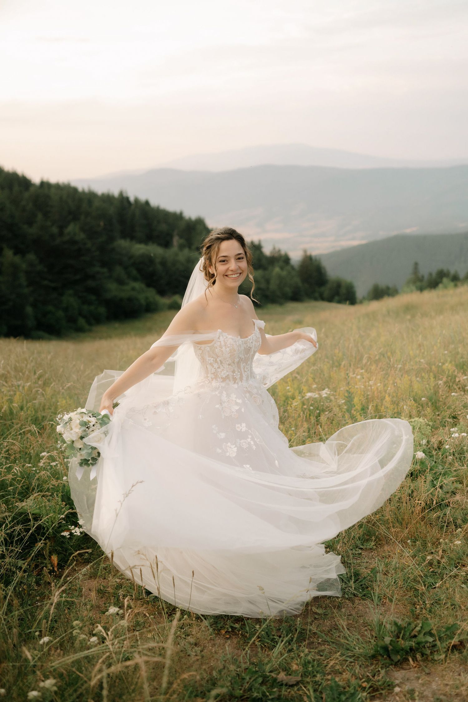 Ethereal bridal portraits show a flowing white gown dancing in the wind against a scenic mountain landscape.