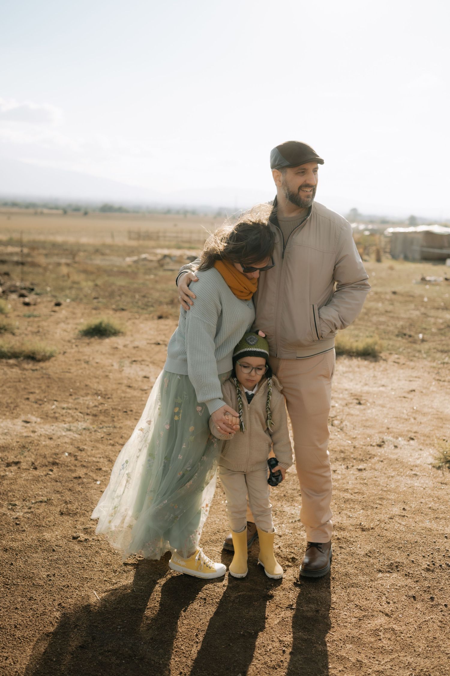 Two people in warm clothing stand together in a barren winter landscape during golden hour.